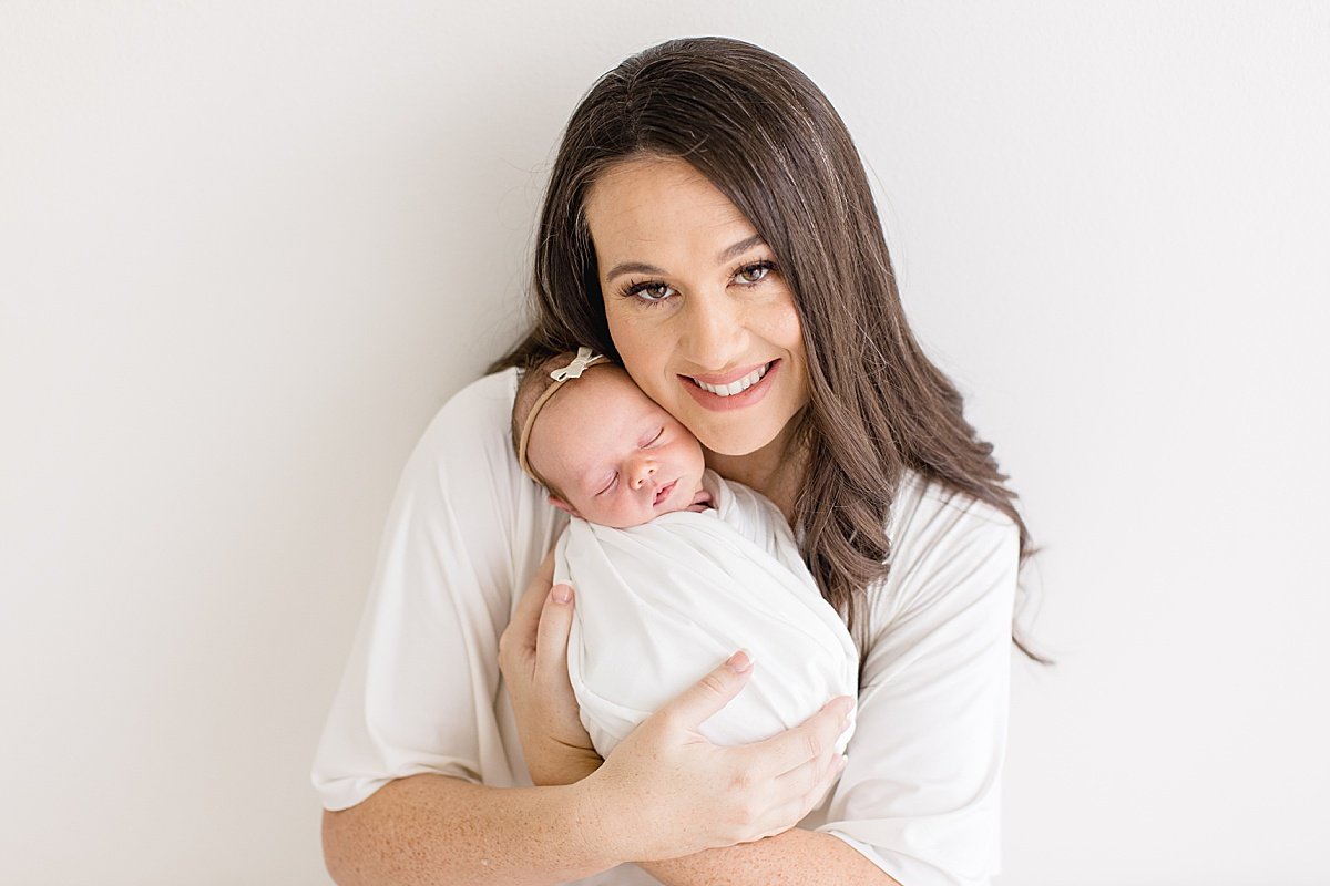 Mom hugs her newborn baby girl while smiling at Newport Beach Studio with Ambre Williams Photography