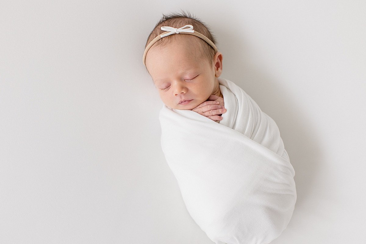 Newborn baby girl swaddled up in white blanket during portrait session with Ambre Williams in her Newport Beach studio
