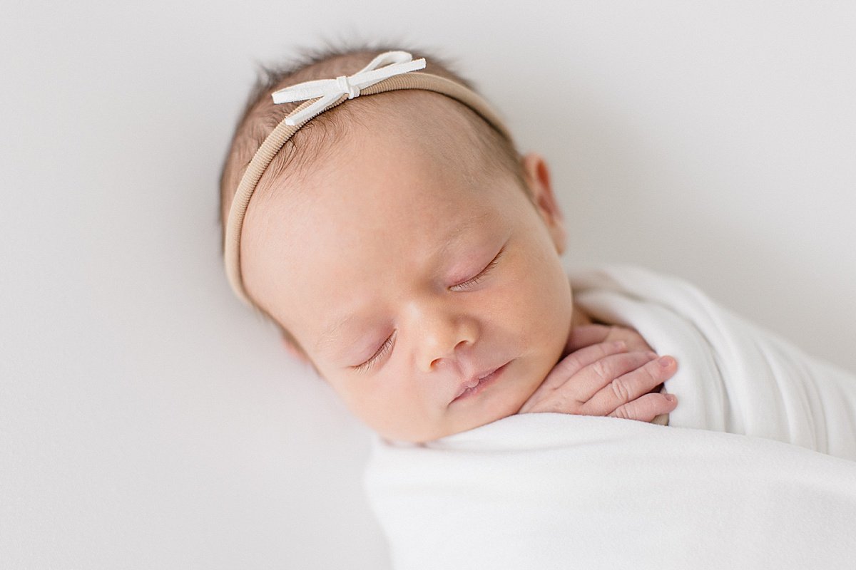 Little Baby girl wearing bow headband swaddled in white blanket | Newport Beach studio with Ambre Williams photography