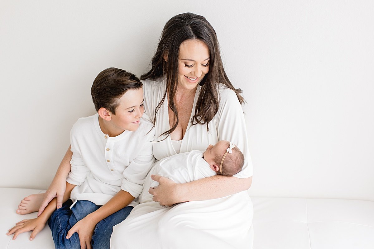 Oldest brother and mom carrying her little daughter on the couch | Newborn Session with Ambre Williams in Newport Beach Studio