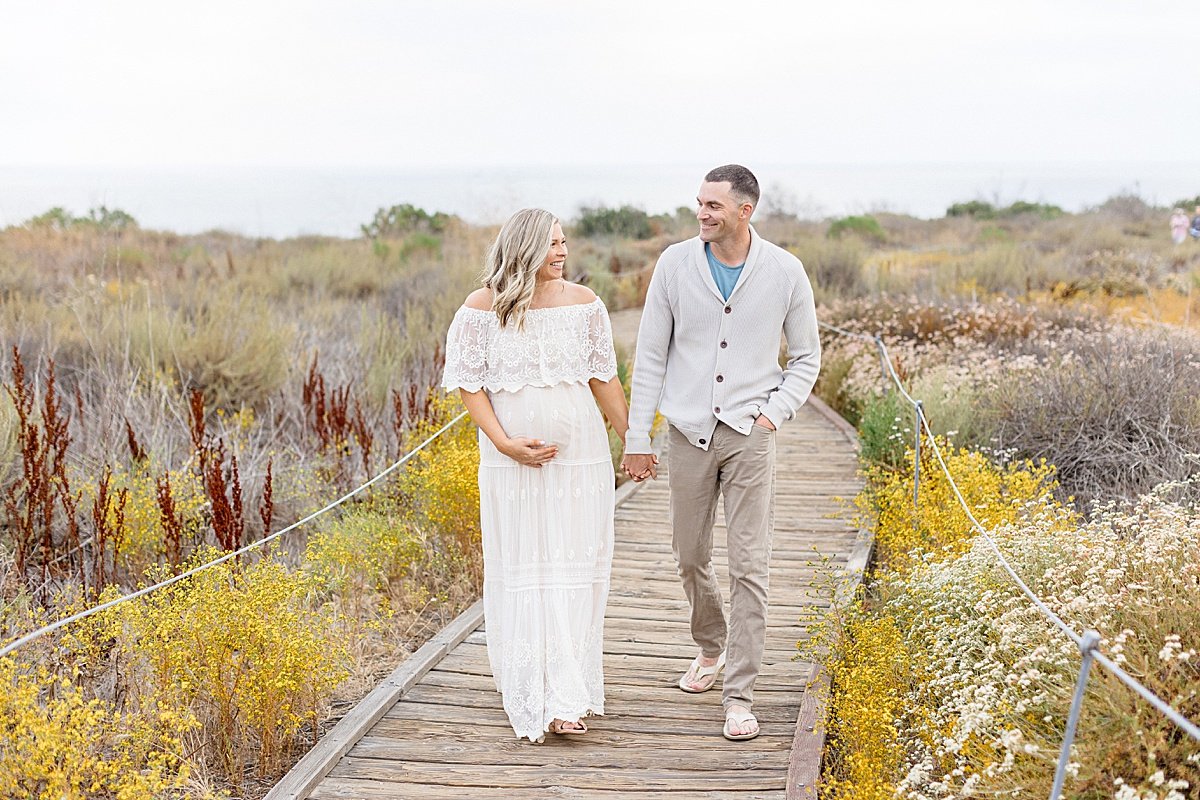 Husband and Wife walking during beach pathway during portrait session | Maternity Shoot with Ambre Williams Photography