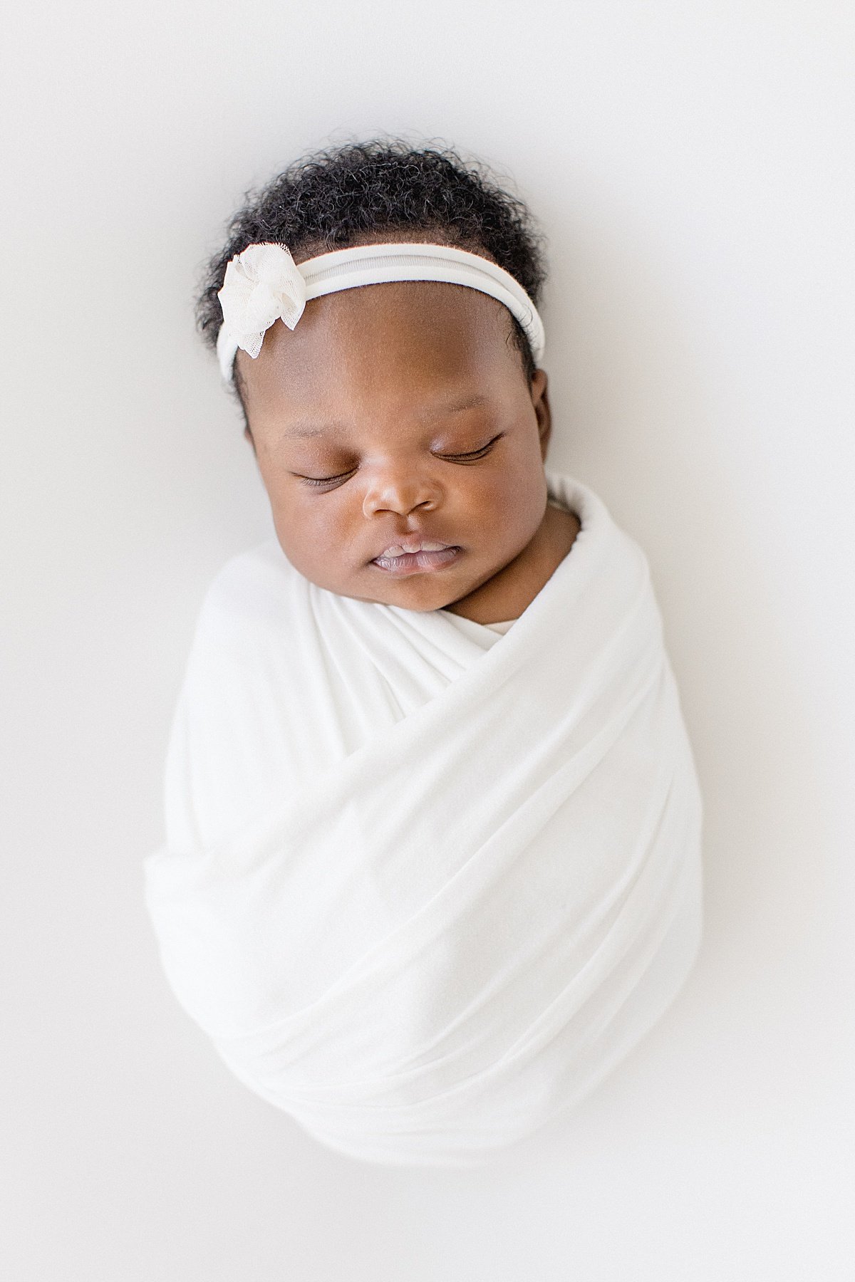 sleepy newborn baby swaddled tight with a small hair bow | Ambre Williams Photography in Newport Beach