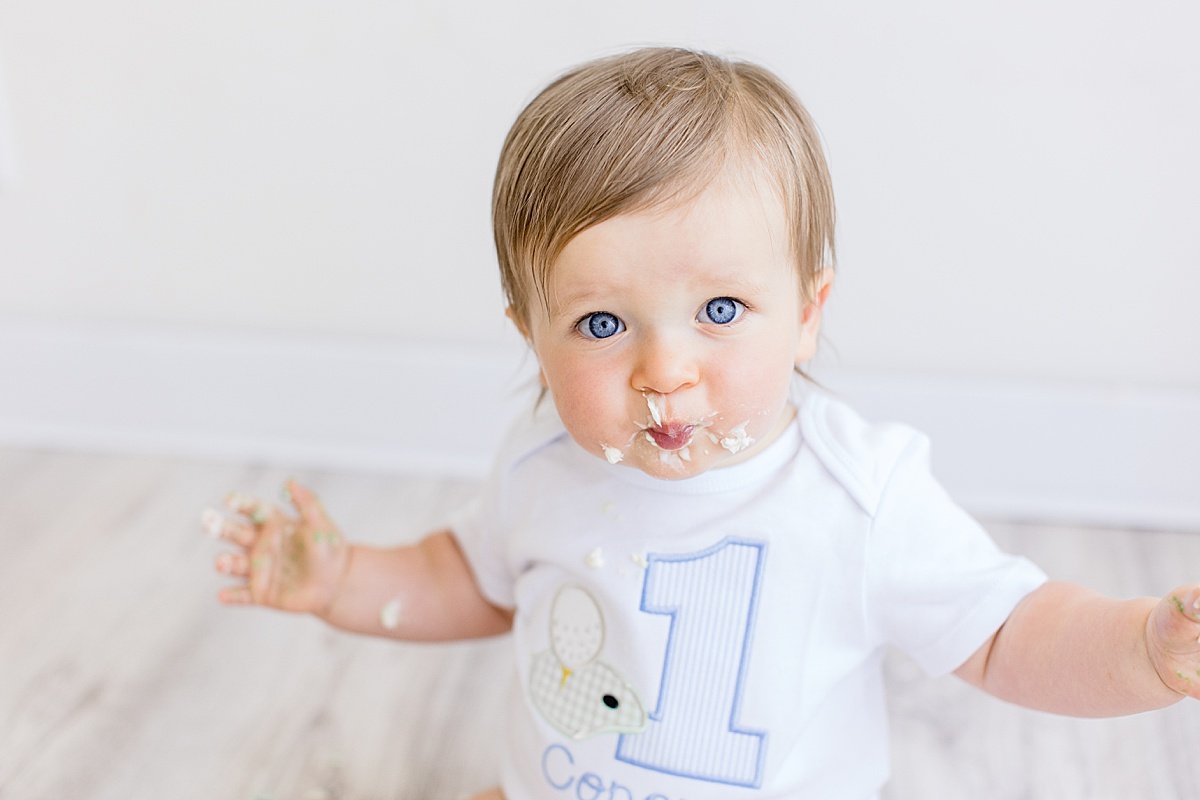 Happy baby eating birthday cake during cake smash with Ambre Williams photography in Newport Beach Studio