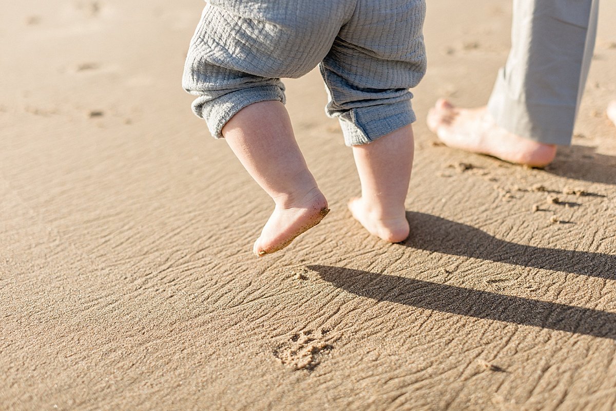 Candid photo of baby walking on sand during beach session with Ambre Williams Photography in California