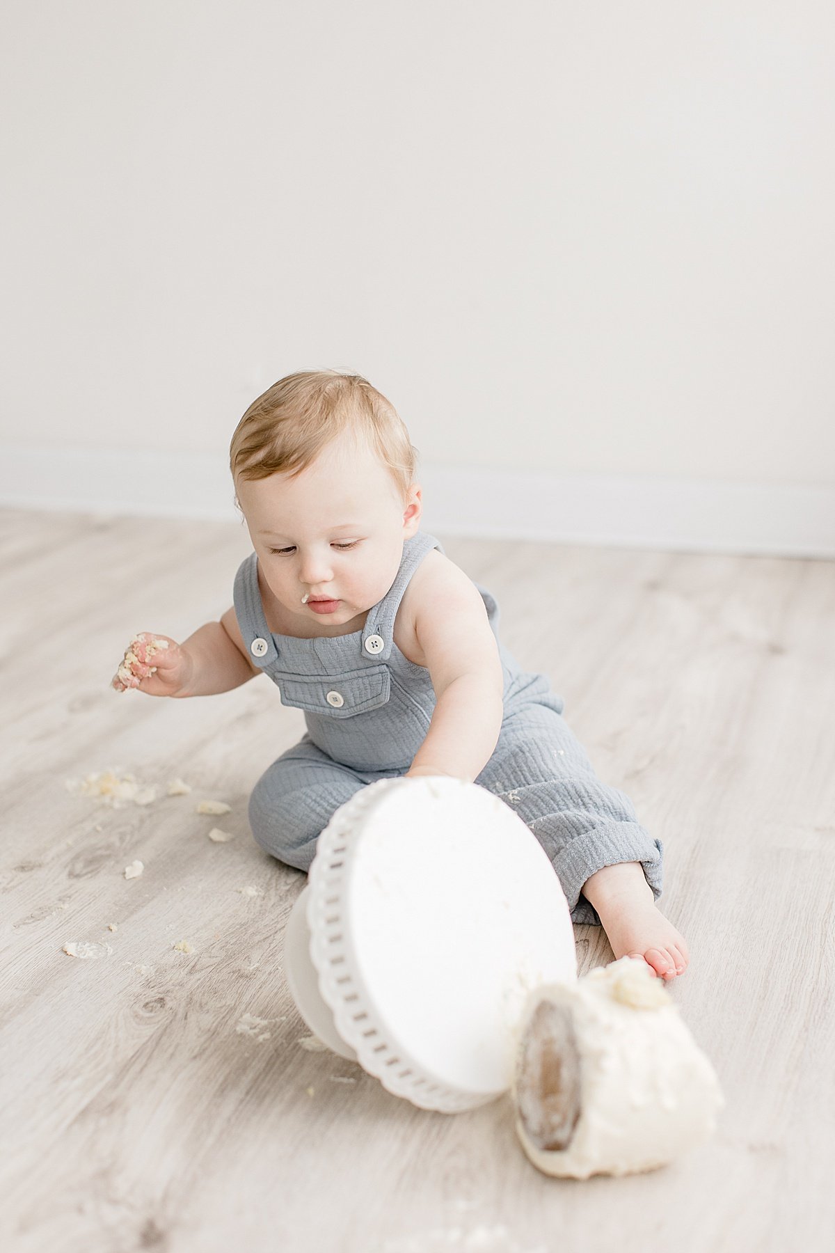 Candid photo of one year old knocking over smash cake in studio session with Ambre Williams Photography