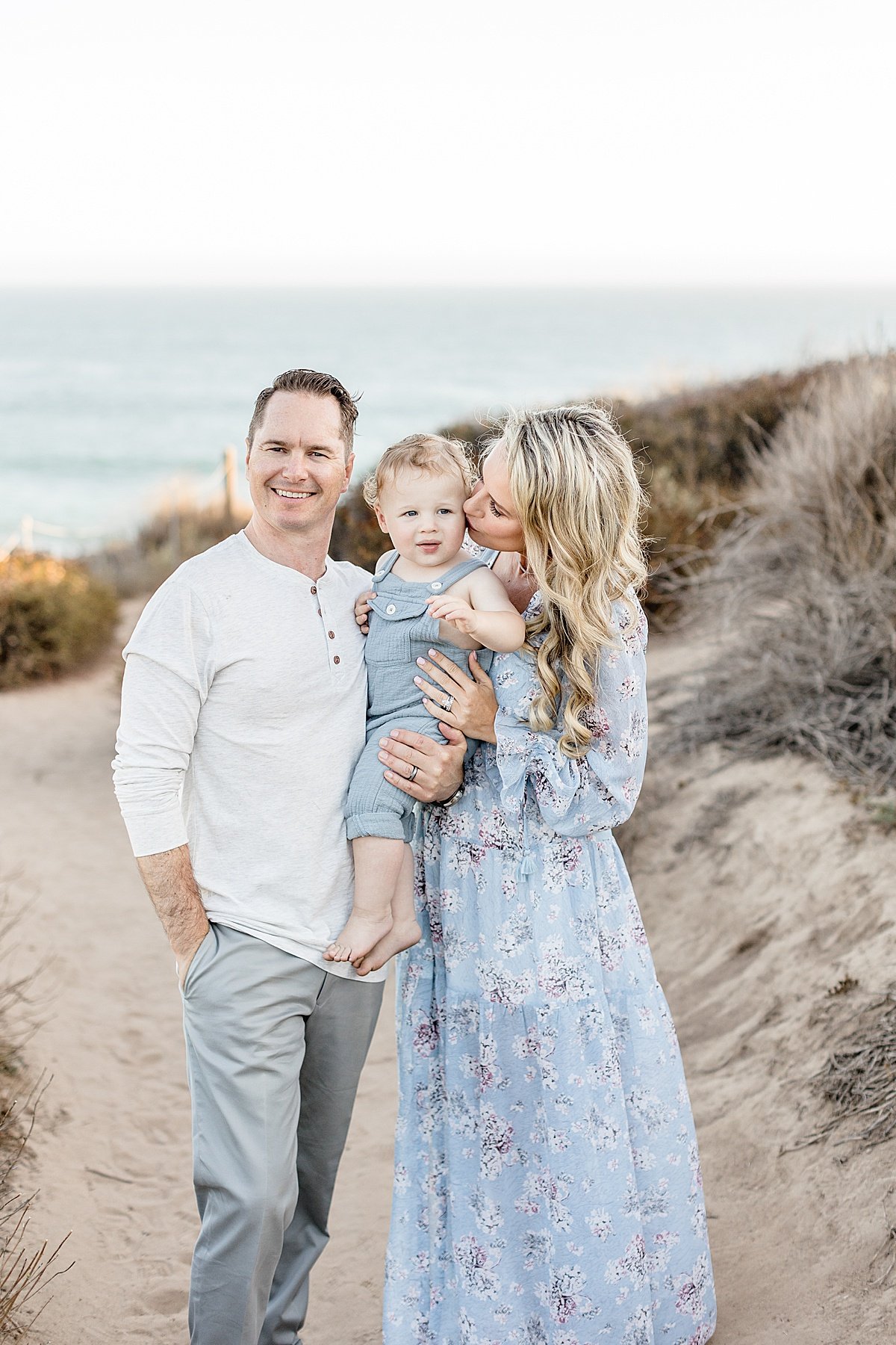 Mom kissing baby boy on Beach, Dad holding Baby during Sunset | Ambre Williams Photography in Newport Beach, California