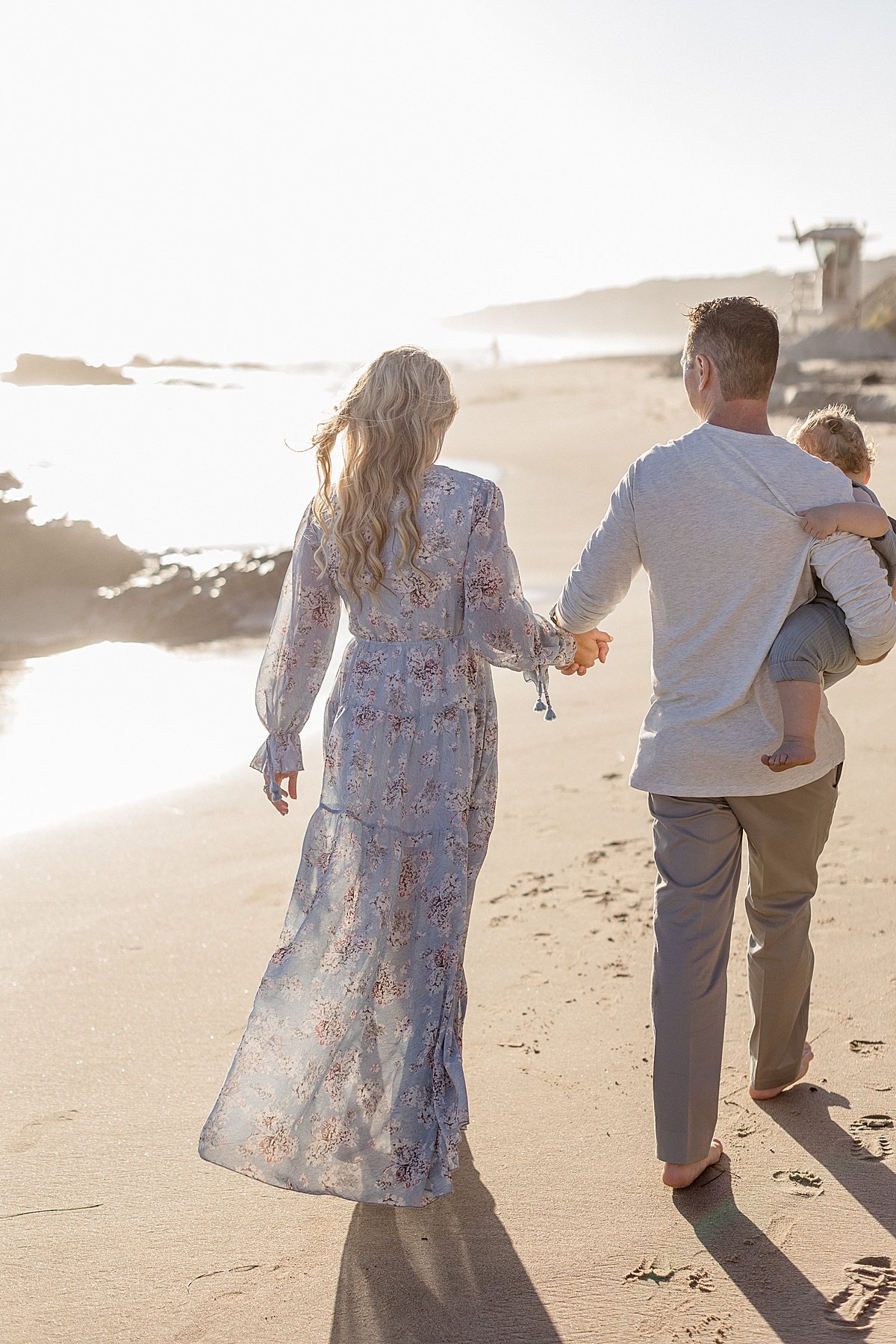 Husband and Wife holding hands walking on beach during on sunset with Baby Boy in arm | Ambre Williams Photography, California Photographer