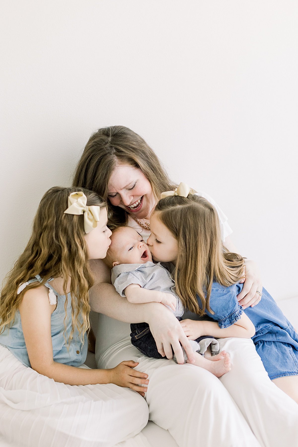 Grandma and Grand daughters kissing little baby brother during during milestone portrait session with Ambre Williams Photography in Newport Beach