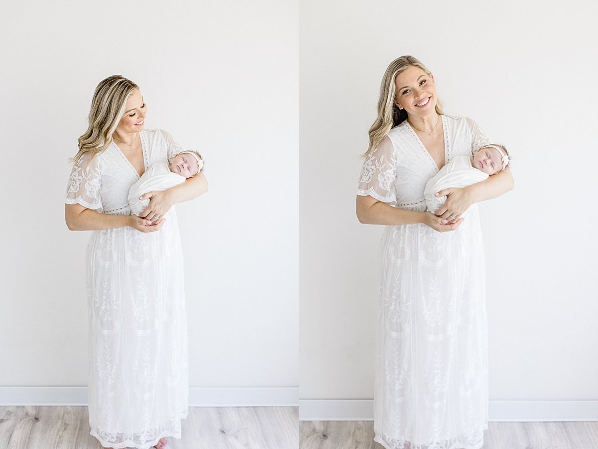 Mom soothing newborn baby girl in beautiful white dress during portrait session in studio with Ambre Williams in California.