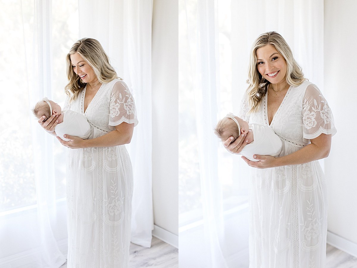 Mom at window holding her newborn baby girl during newborn signature session with Ambre Williams Photography in Newport Beach