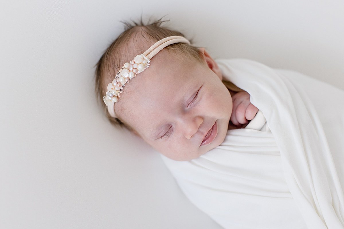 Smiling sleepy baby girl wearing white rhinestone headband | Ambre Williams Photography in Newport Beach California