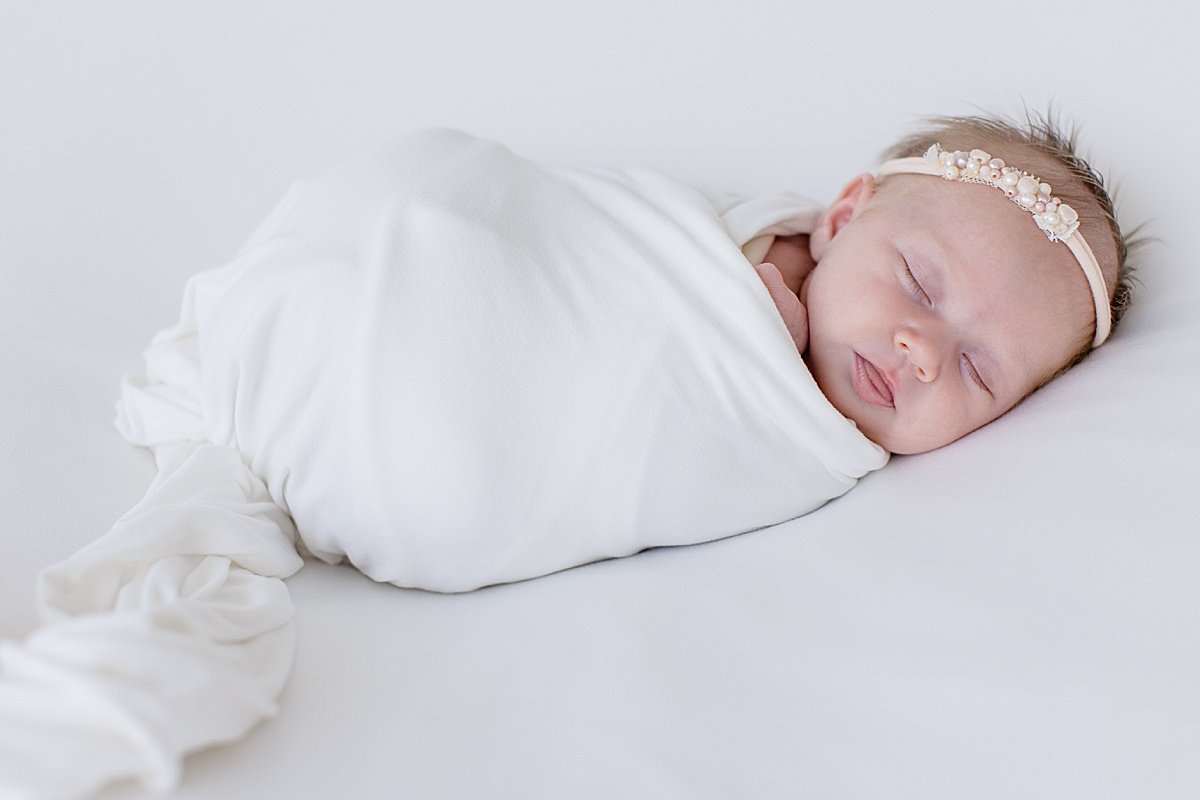 newborn daughter sleeping wrapped up in white linen and rhinestone headband | Ambre Williams Photography