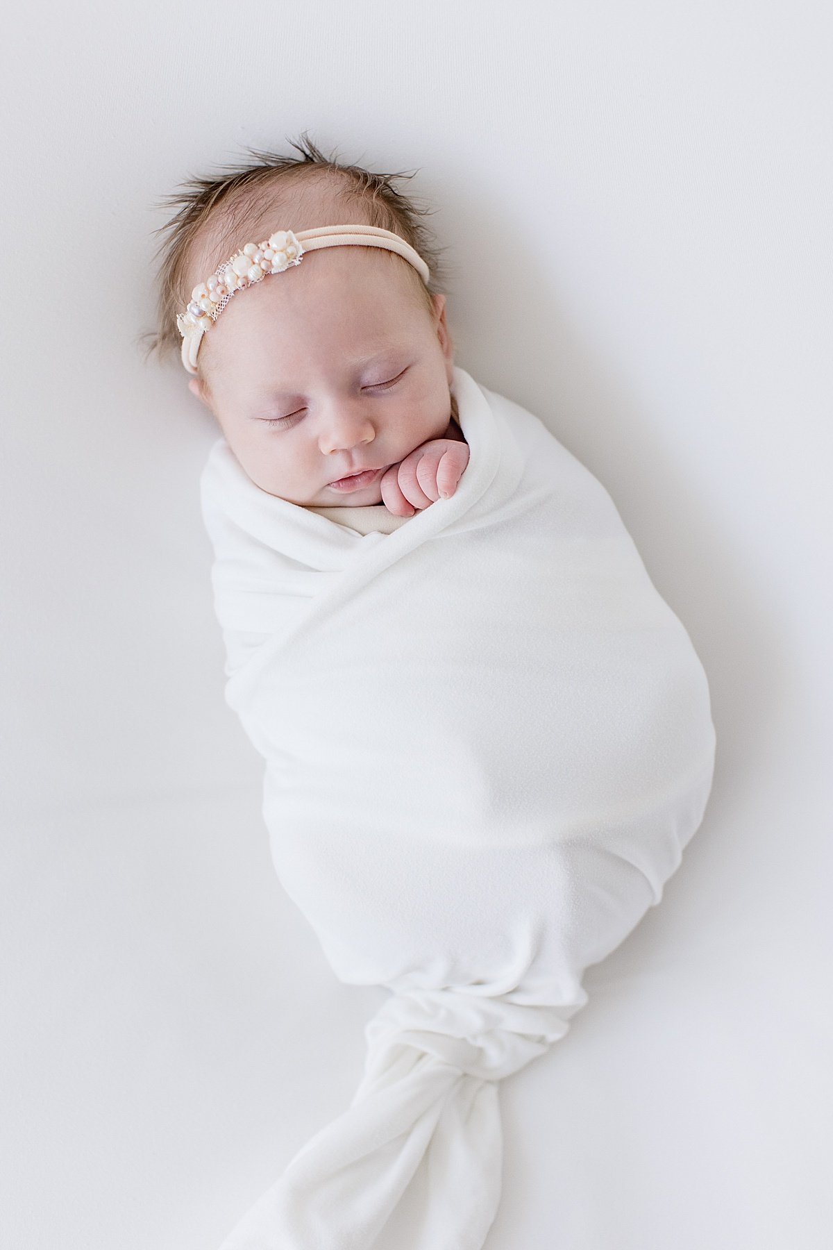 sleepy baby girl wrapped up in white linen during portrait session in Newport Beach California