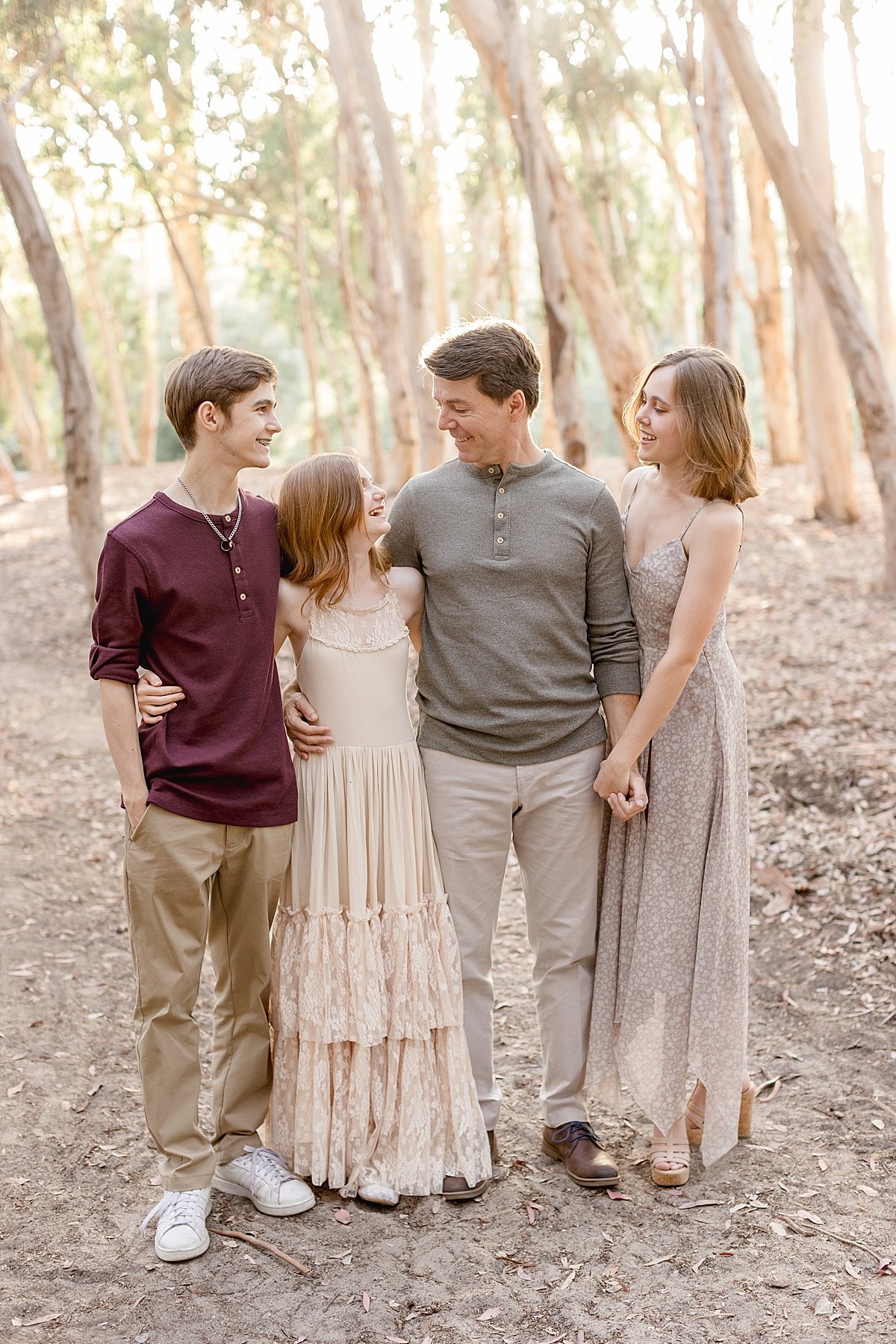 Dad looking at kids smiling during portrait session outdoors in forest wooded trees with Ambre Williams Photography