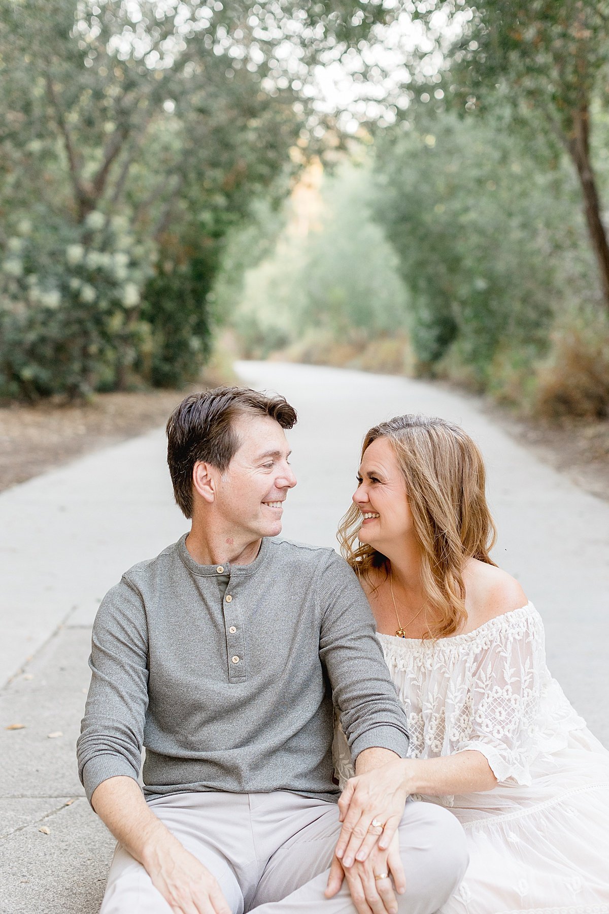 Mom and dad posing together in wooded tree area | happy couple smiling together with Ambre Williams Photography in Newport Beach California