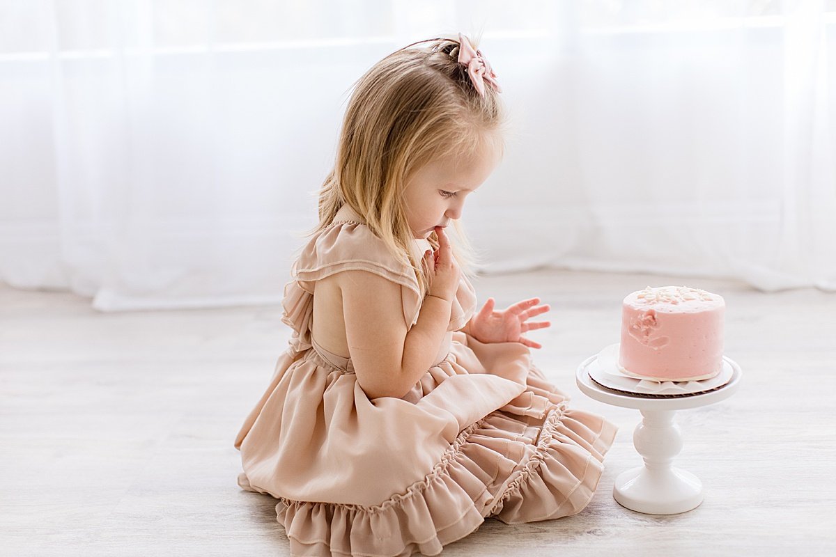 2-year old daughter looking at smash cake during birthday session with Ambre Williams Photography in Newport Beach