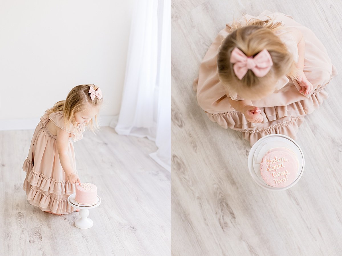 2 year old daughter looking at pink smash cake during photography session with Ambre Williams in Newport Beach California