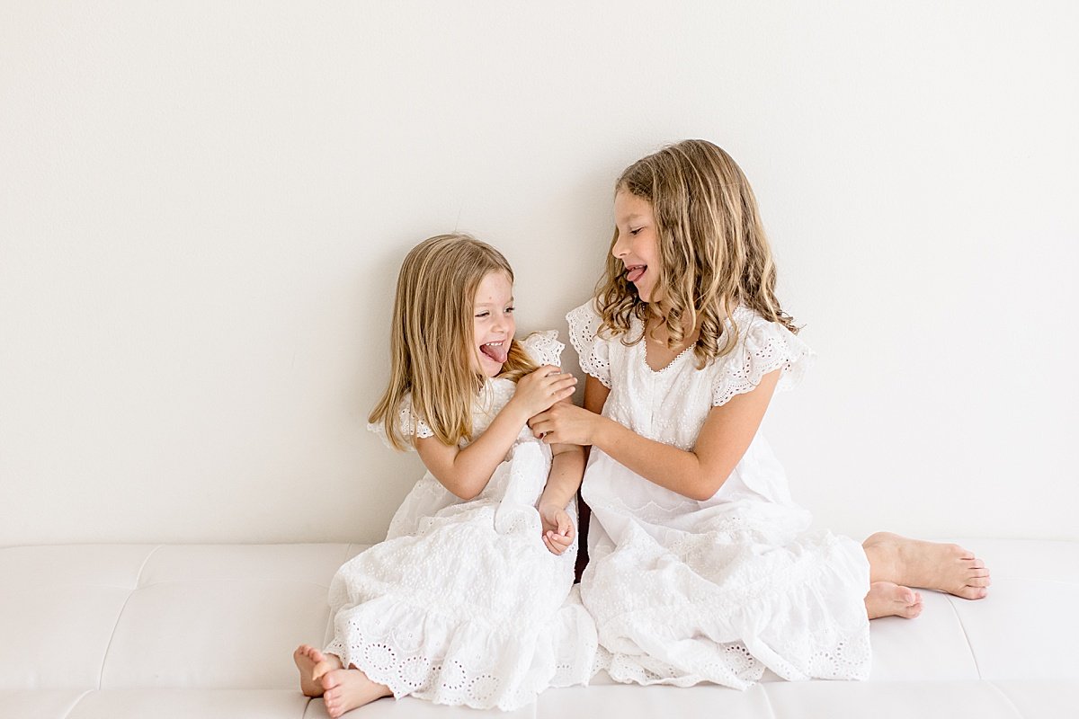 Sisters laughing together on couch during portrait session with Ambre Williams Photography in Newport Beach California photography studio