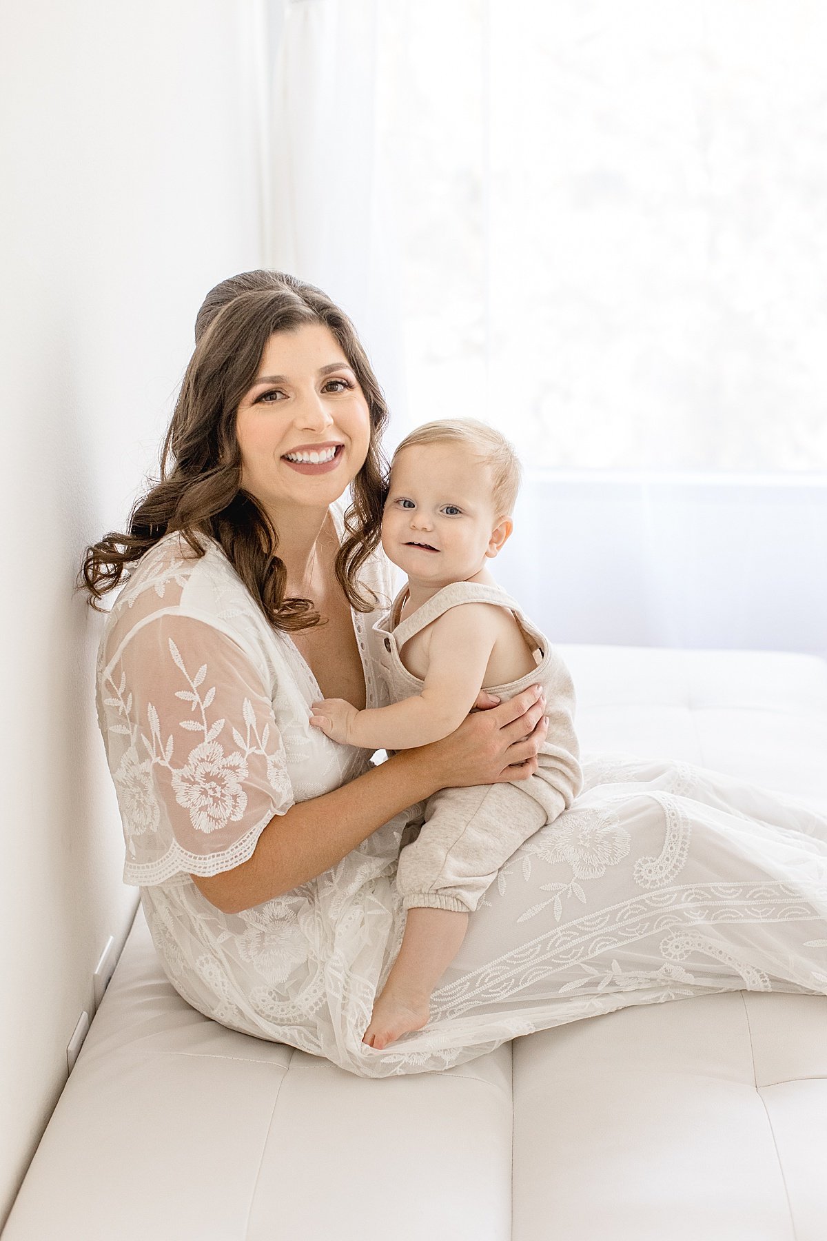 Mom and baby sitting together on white couch during portrait session for first year at Newport Beach studio with Ambre Williams Photography