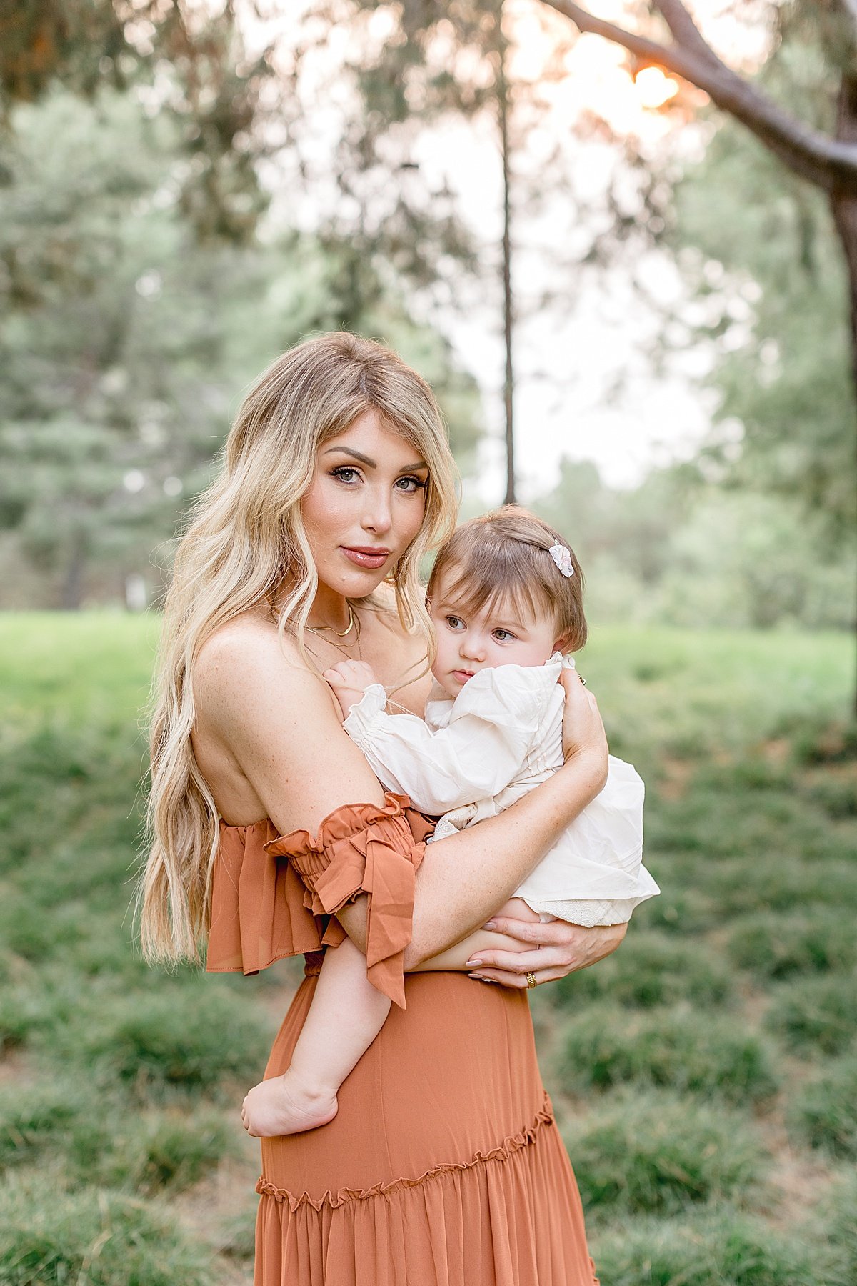 Beautiful momma in orange holding daughter in forest during outdoor fall portrait session with Ambre Williams Photography