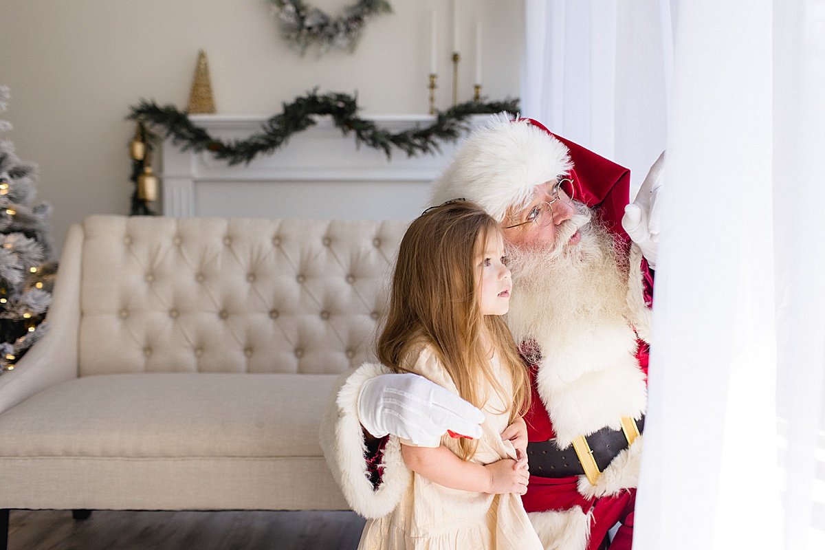 Santa looking outside window with small child in studio with Ambre Williams Photography during Santa's Magical Experience in Newport Beach