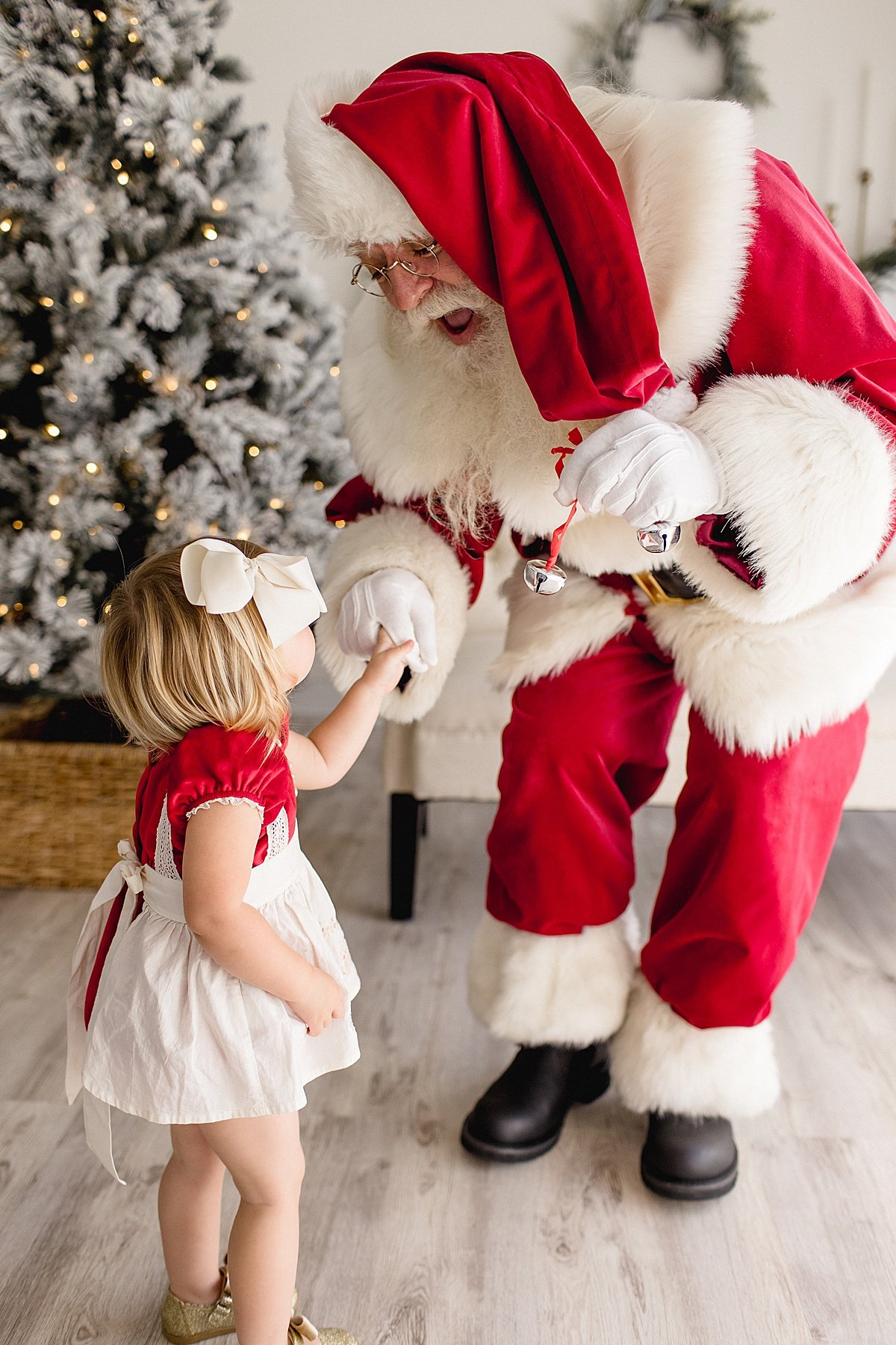 Santa helping young girl hang holiday ornament on Christmas tree during Santa's Magical Experience with Ambre Williams Photography