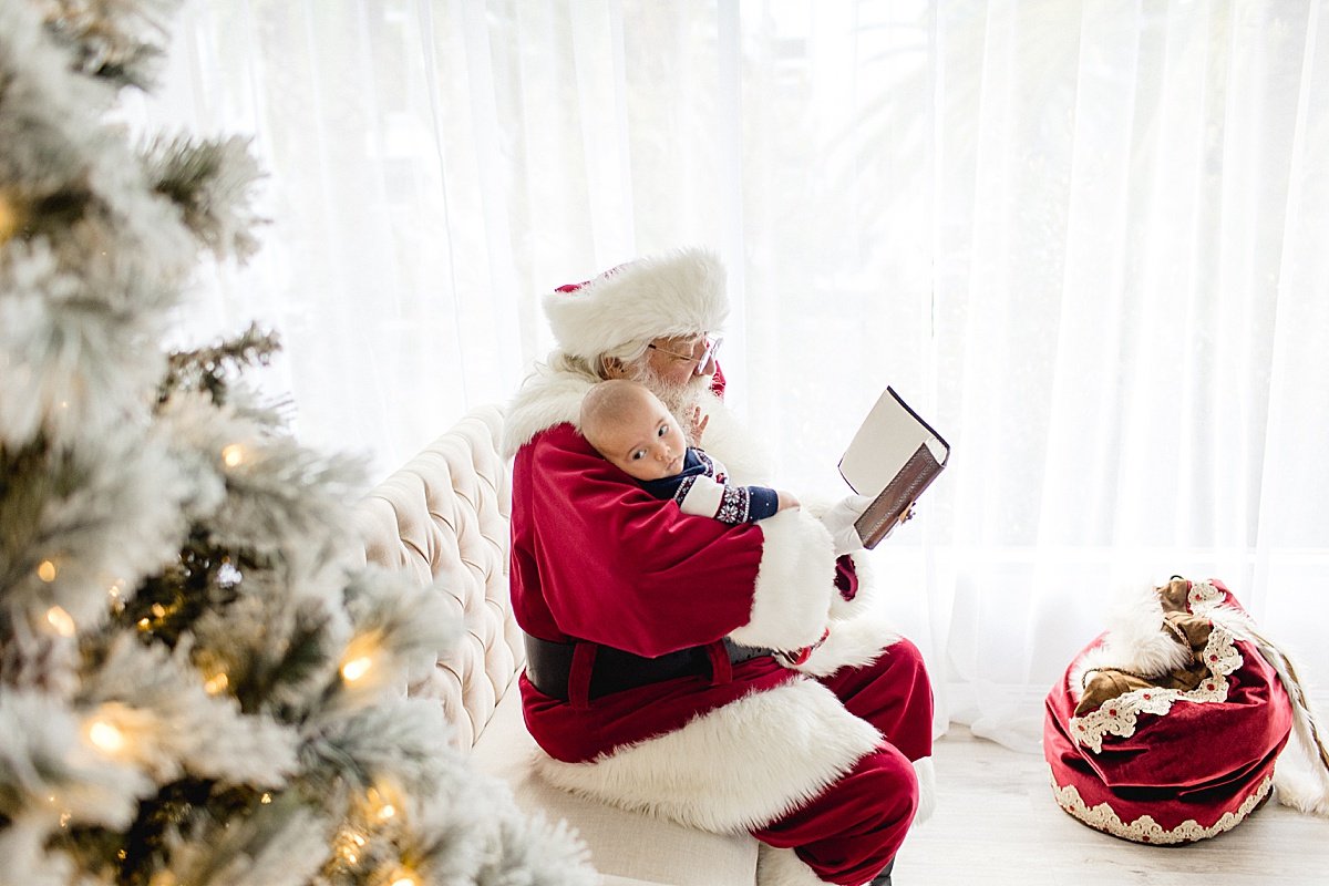 Santa reading baby a story while rocking him to sleep during Santa's Magical Experience with Ambre Williams Photography in Newport Beach studio | Holiday Magic Session