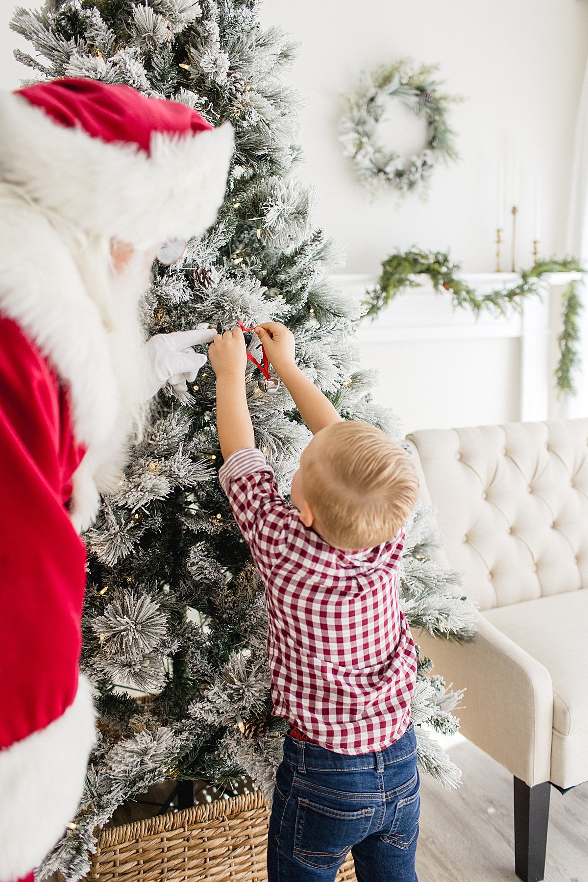 Candid photo of Santa helping young boy hang ornament on Christmas tree during Santa's Magical Experience during Newport Beach studio session with Ambre Williams Photography