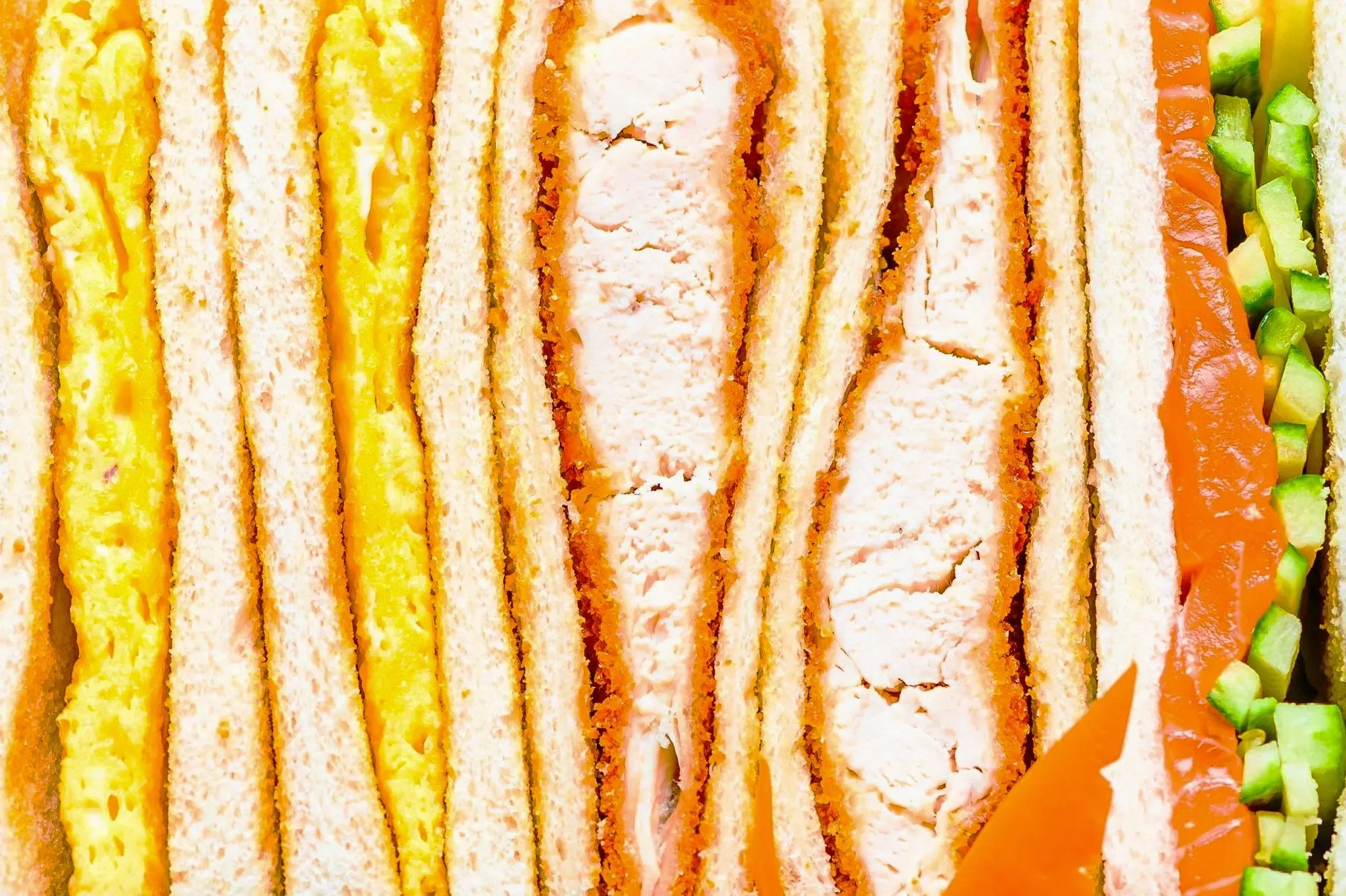 Close-up of multiple layered sandwiches, including egg salad, chicken, smoked salmon, and vegetables.