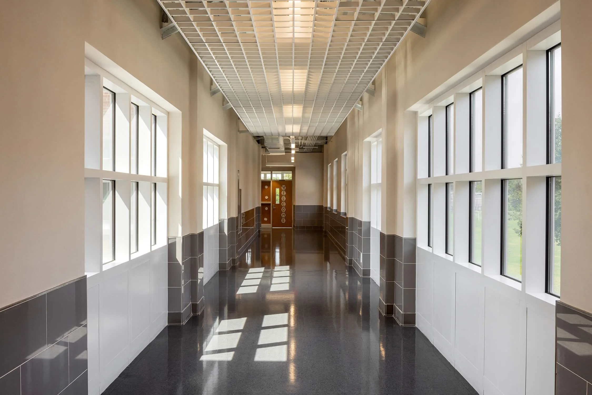 School corridor with reflective dark floor, wall of windows and natural light at the end of the hall, Brian Berkowitz Photography Long Island