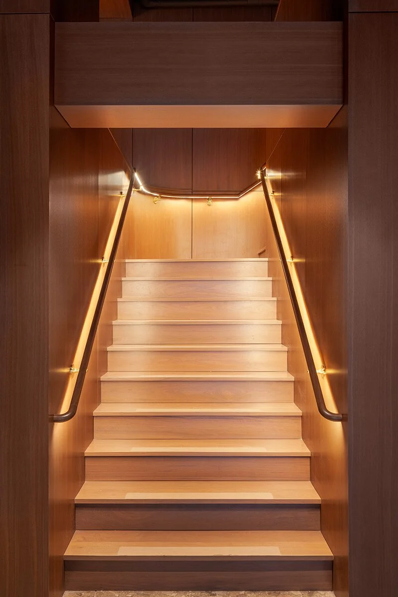 Warmly lit staircase with wood paneling and brass handrails at TMPL fitness club