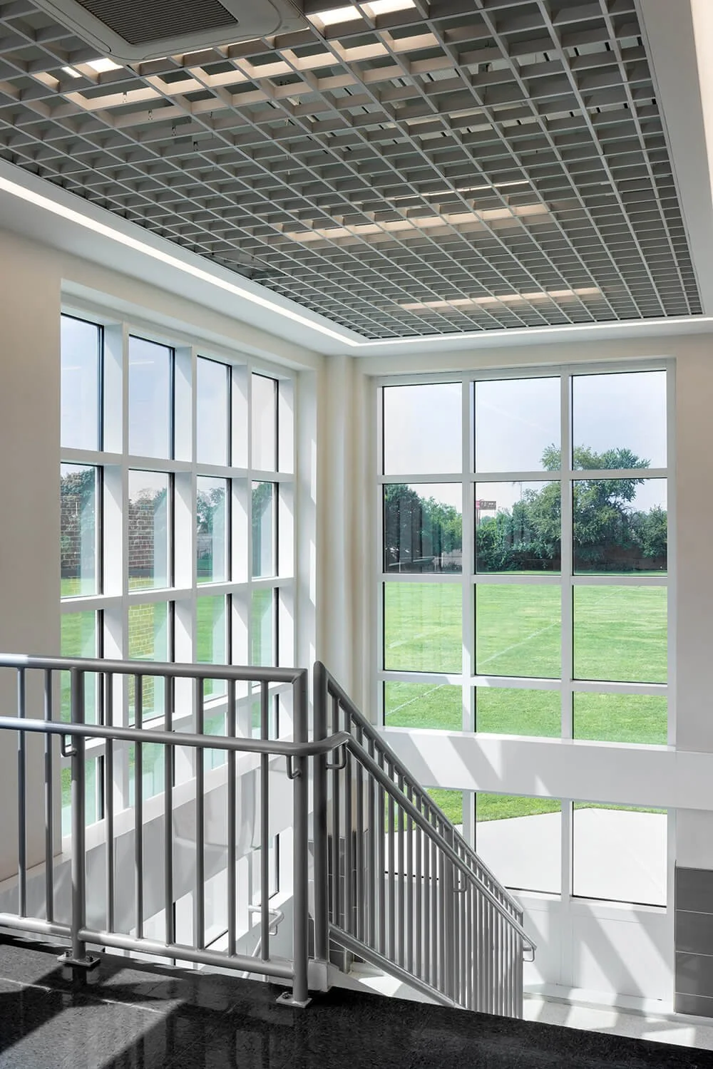 School interior corner with geometric glass grid ceiling, ramp railing and large windows overlooking athletic field, Brian Berkowitz Photography Long Island