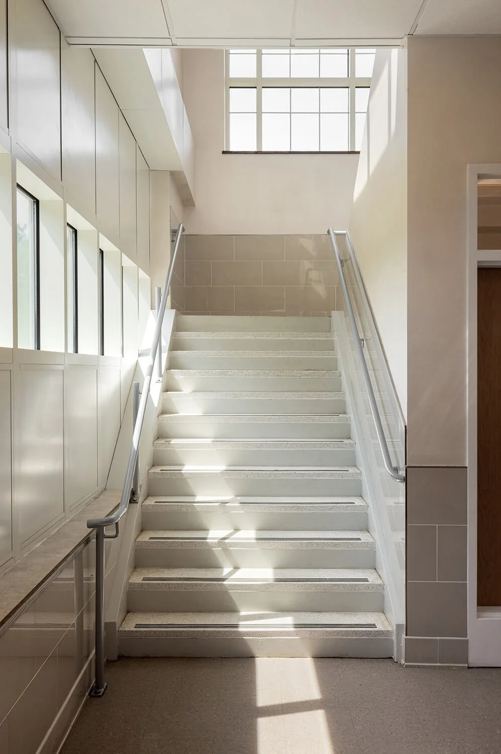 School staircase with dramatic natural light and shadow patterns on white steps and glass railing, Brian Berkowitz Photography Long Island