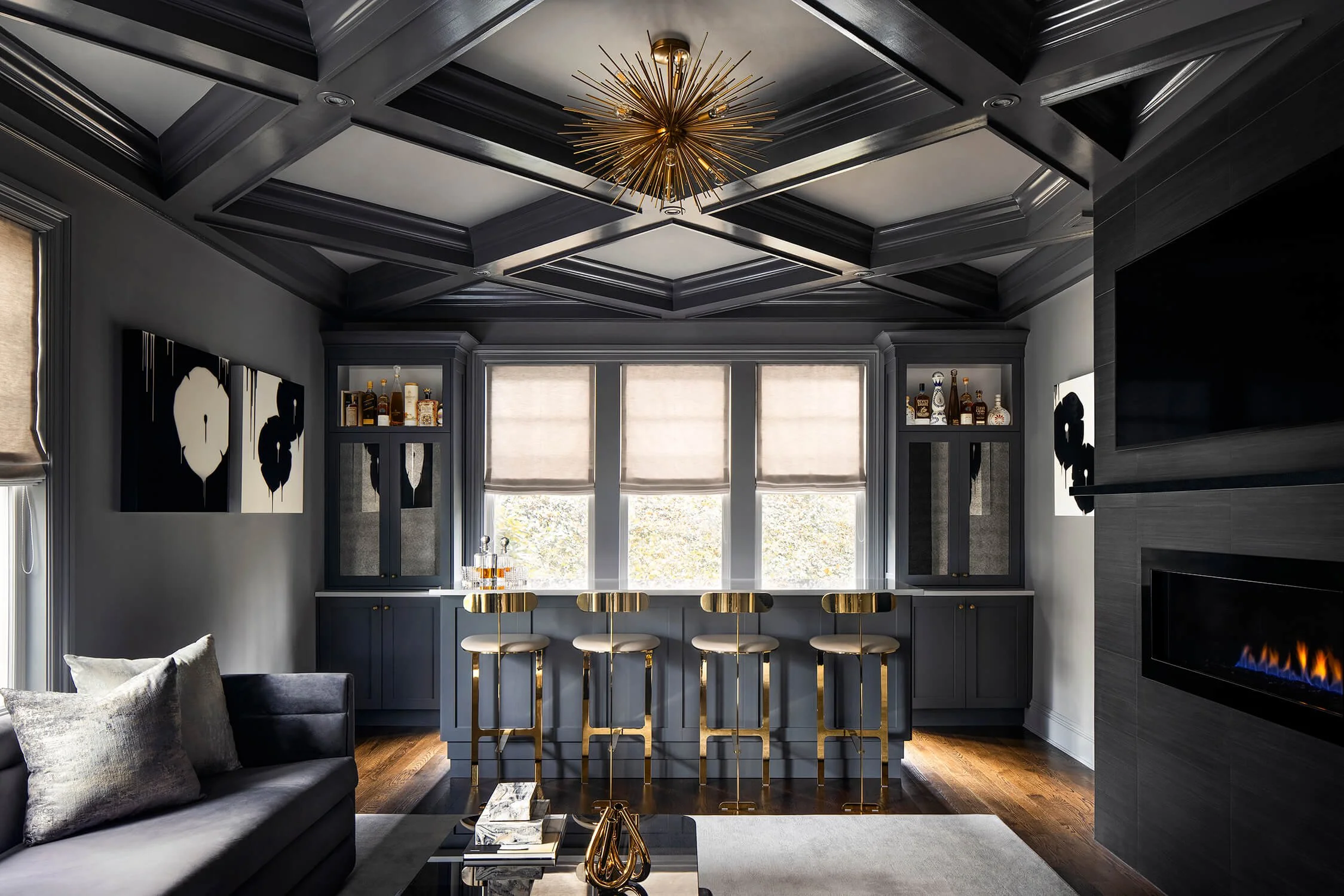 Dramatic bar room and living space with dark coffered ceilings, gold bar stools, fireplace, and built-in shelving, designed by Stacey Marks, photographed by Brian Berkowitz Photography on Long Island