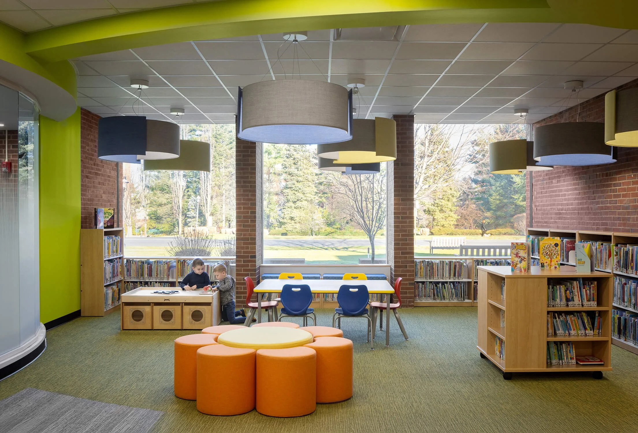 Children's library with green accent walls, orange ottomans, brick columns and natural light, education photography by Brian Berkowitz Photography