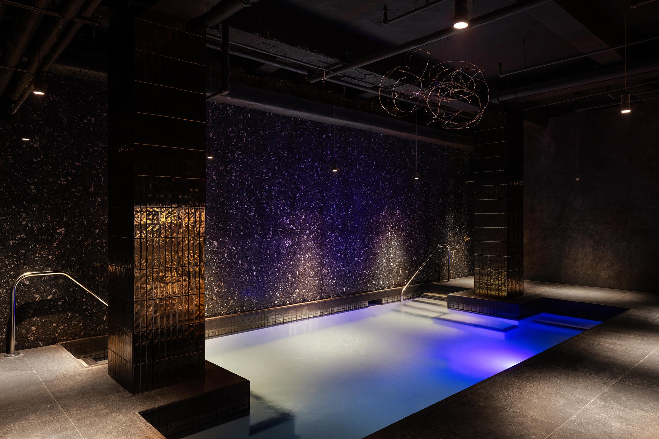 Indoor spa pool with moody lighting and reflective black tile walls