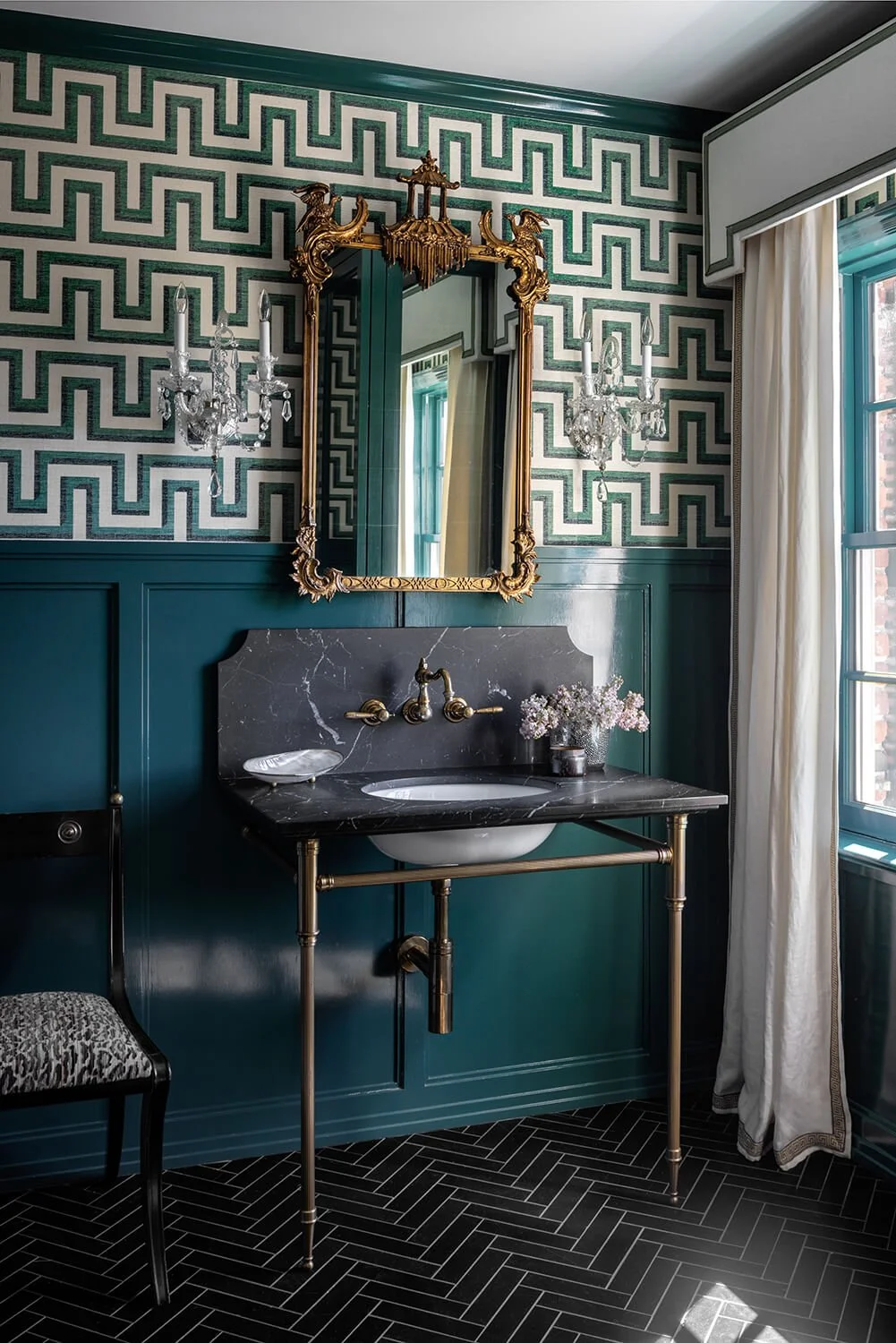 Powder room with deep teal board and batten millwork, Greek key wallpaper, gold mirror, black marble washstand, and herringbone tile floor, photographed by Brian Berkowitz Photography on Long Island