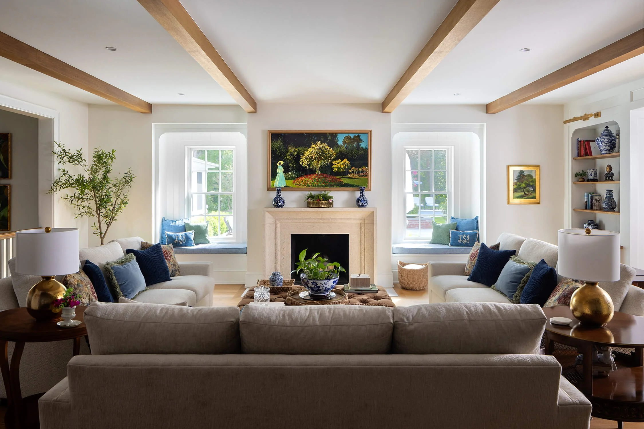Symmetrical living room with exposed wood ceiling beams, flanking upholstered window seats, stone fireplace, and blue and white decor, photographed by Brian Berkowitz Photography on Long Island