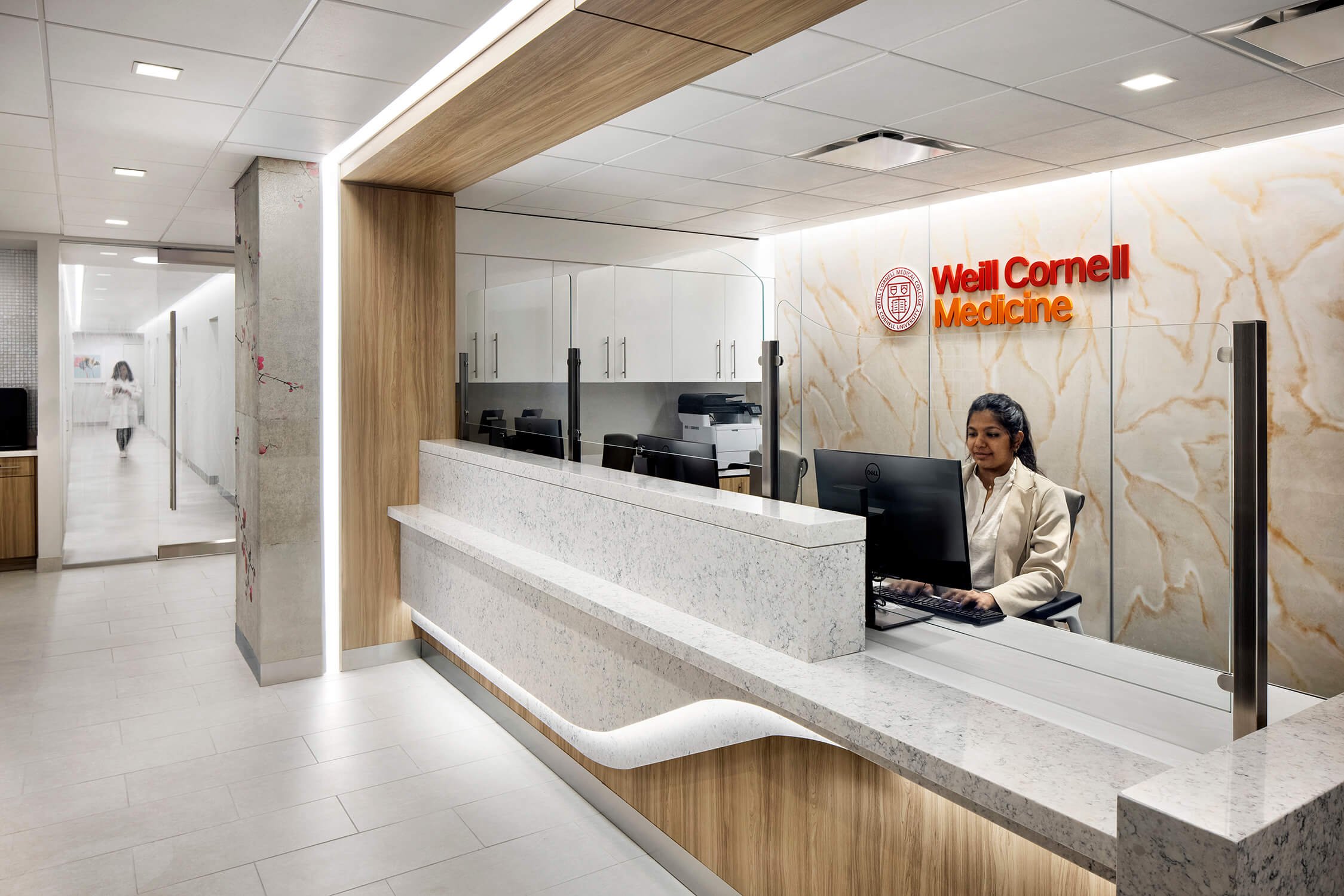 Weill Cornell Medicine reception desk with staff member and cherry blossom wall art, healthcare interior photography by Brian Berkowitz Photography NYC