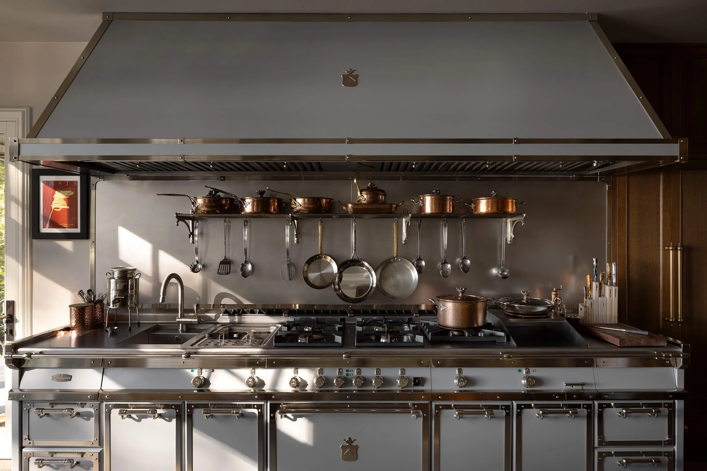 Professional La Cornue range with stainless steel hood, copper pots and pans, hanging utensils, and stainless backsplash shelf, photographed by Brian Berkowitz Photography in New York