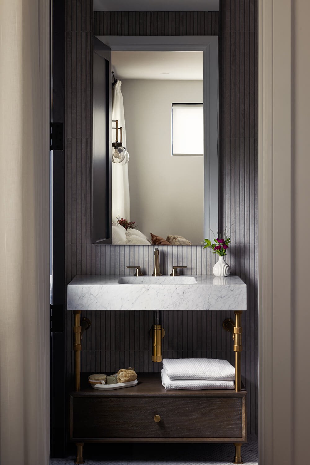 Moody bathroom with dark fluted wall panels, floating marble vanity, brass leg fixtures, and framed doorway composition, photographed by Brian Berkowitz Photography on Fire Island New York