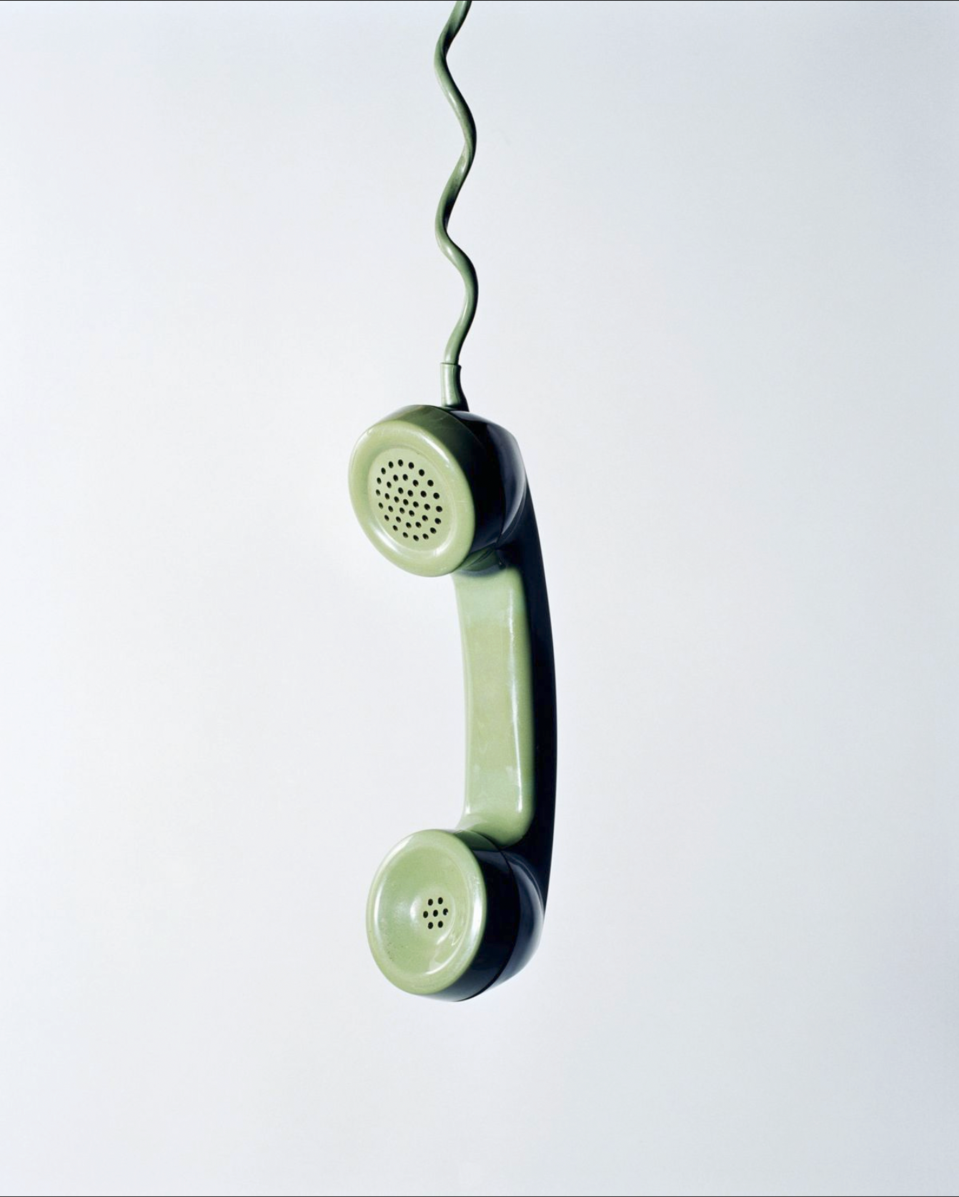 Vintage green telephone handset hanging against a plain background.