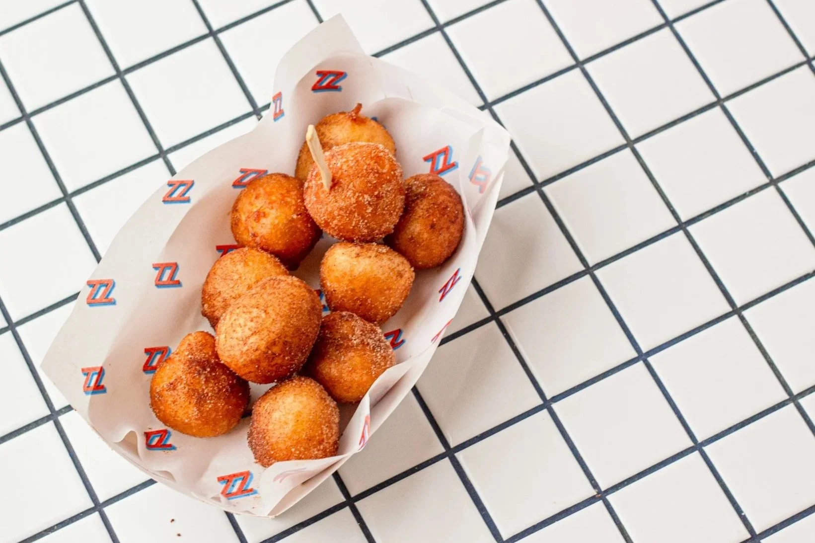 Basket of fried mozzarella sticks with a toothpick on a checkered white and black surface.