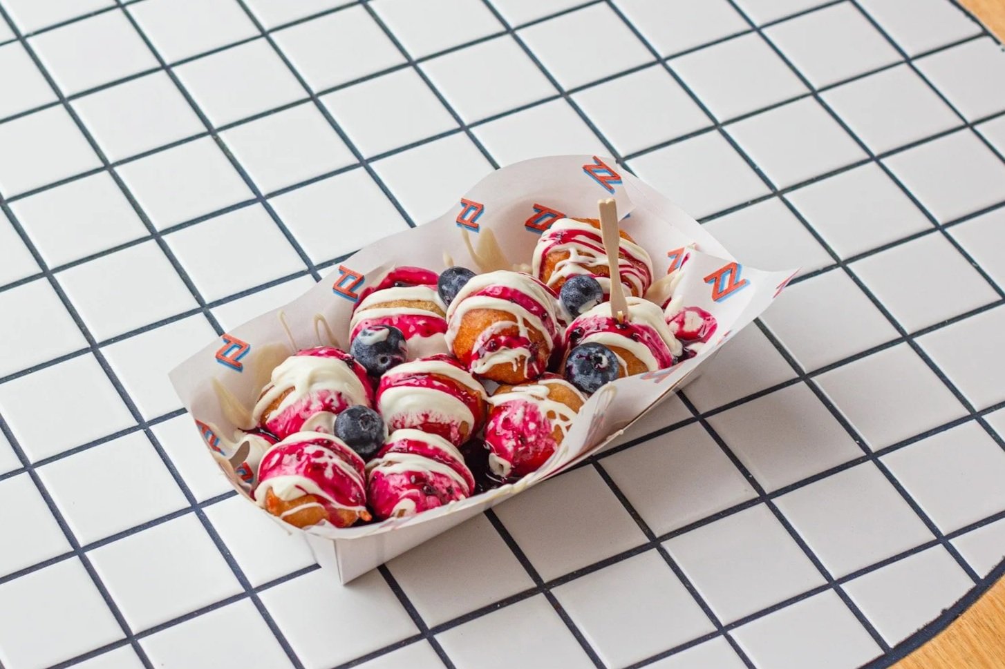 Dessert tray with mini donuts topped with white and red icing and blueberries on a black-and-white checkered surface.
