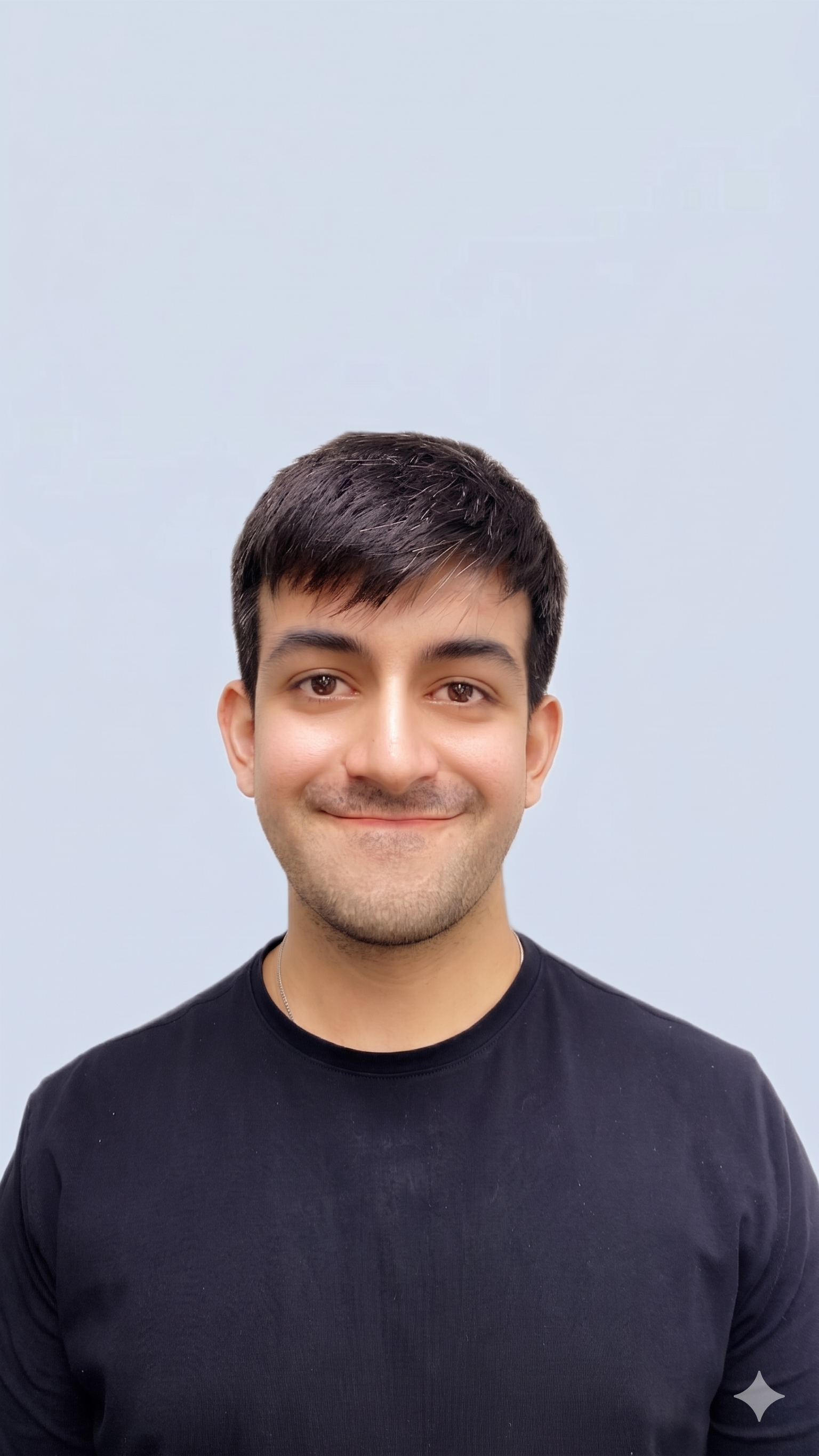 Portrait of a young man with dark hair and a slight smile, wearing a black shirt, standing against a light-colored background.