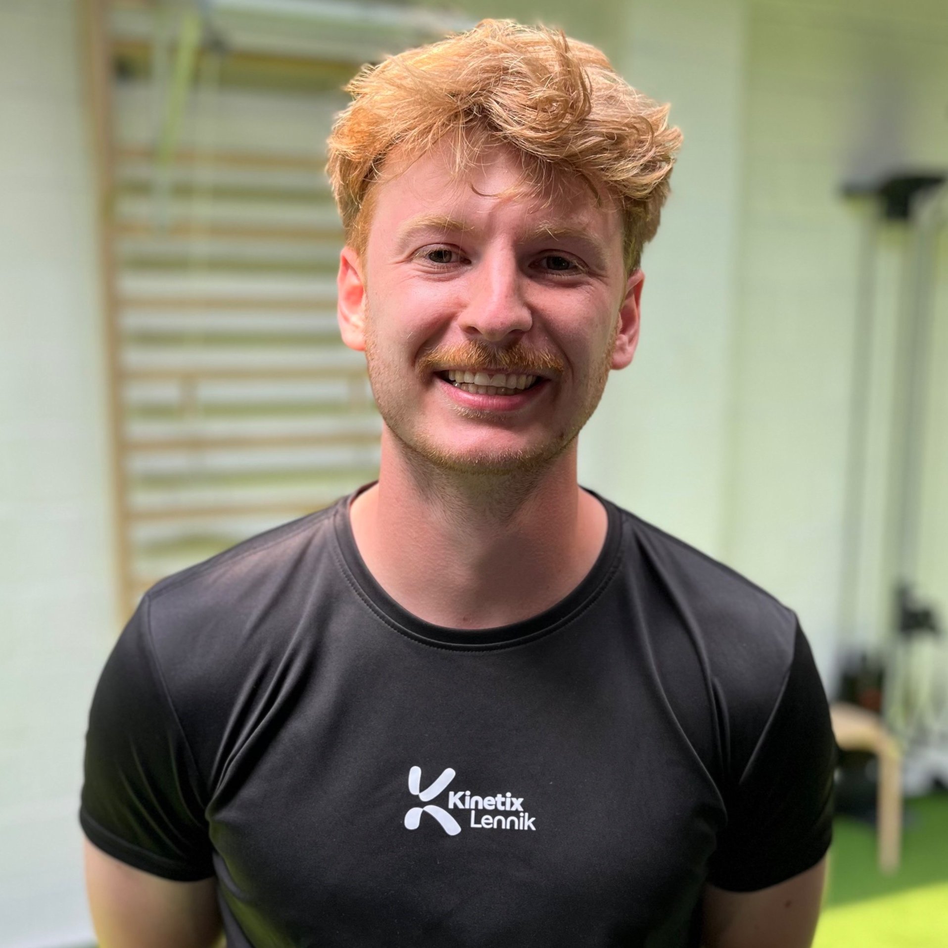 Lachende man in sportkleding met logo 'Kinetix Lennik' in sportschool