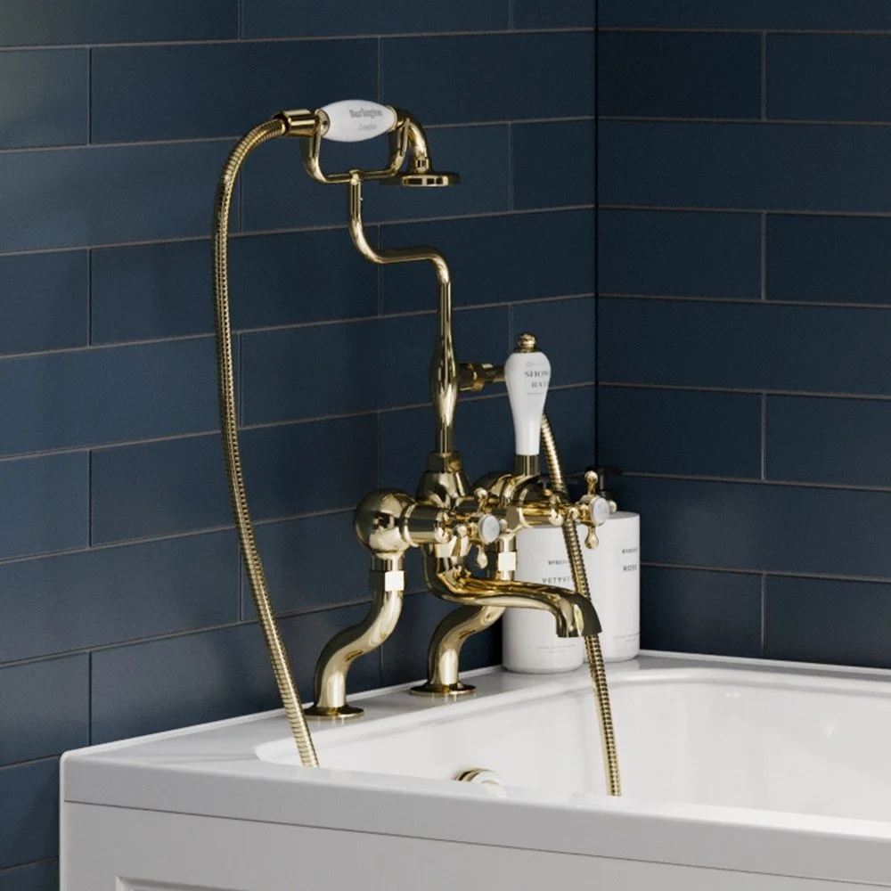 Close-up of a vintage gold bathtub faucet and shower fixture with a dark blue tiled wall background. Classic bathroom taps available at Island Bathrooms Bournemouth and Salisbury
