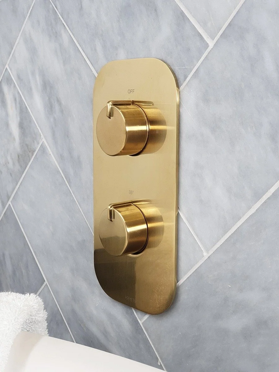 Gold-colored shower temperature and flow control knobs mounted on a tiled bathroom wall. Modern bathroom collection available from Island Bathrooms in Dorset and Wiltshire
