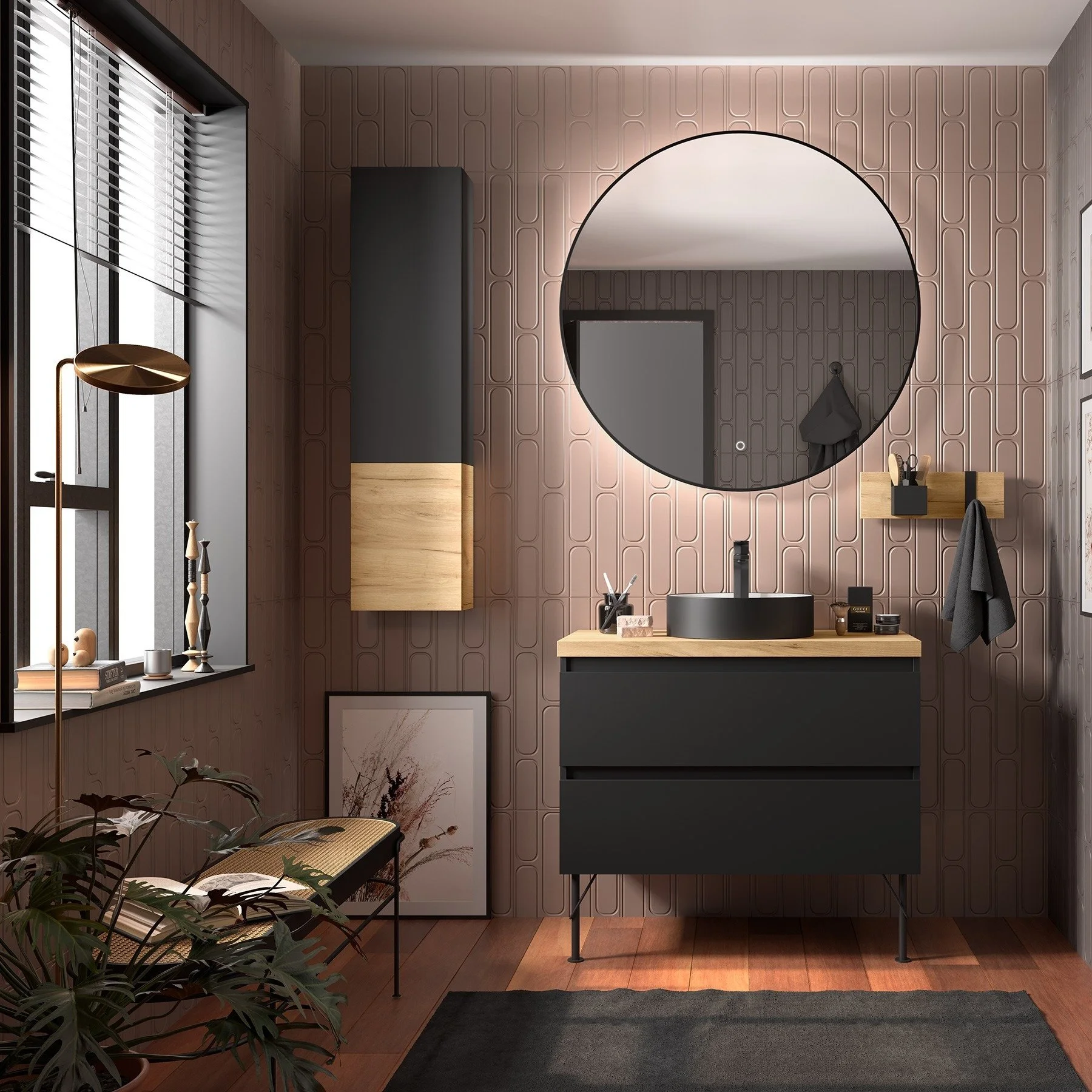 Interior of a modern bathroom with pink textured wall, round mirror, black vanity with black sink, mounted wooden storage, black hooks with gray towel, window with blinds, decorative plants, and artwork. See this bathroom display at Island Bathrooms 