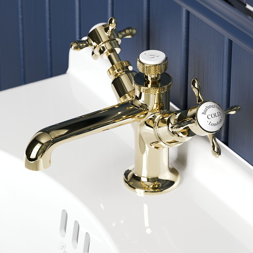 A gold-colored vintage-style bathroom faucet with handles labeled 'Hot' and 'Cold' on a white sink with a blue wooden panel background. Traditional brassware on display at Island Bathrooms Salisbury Wiltshire